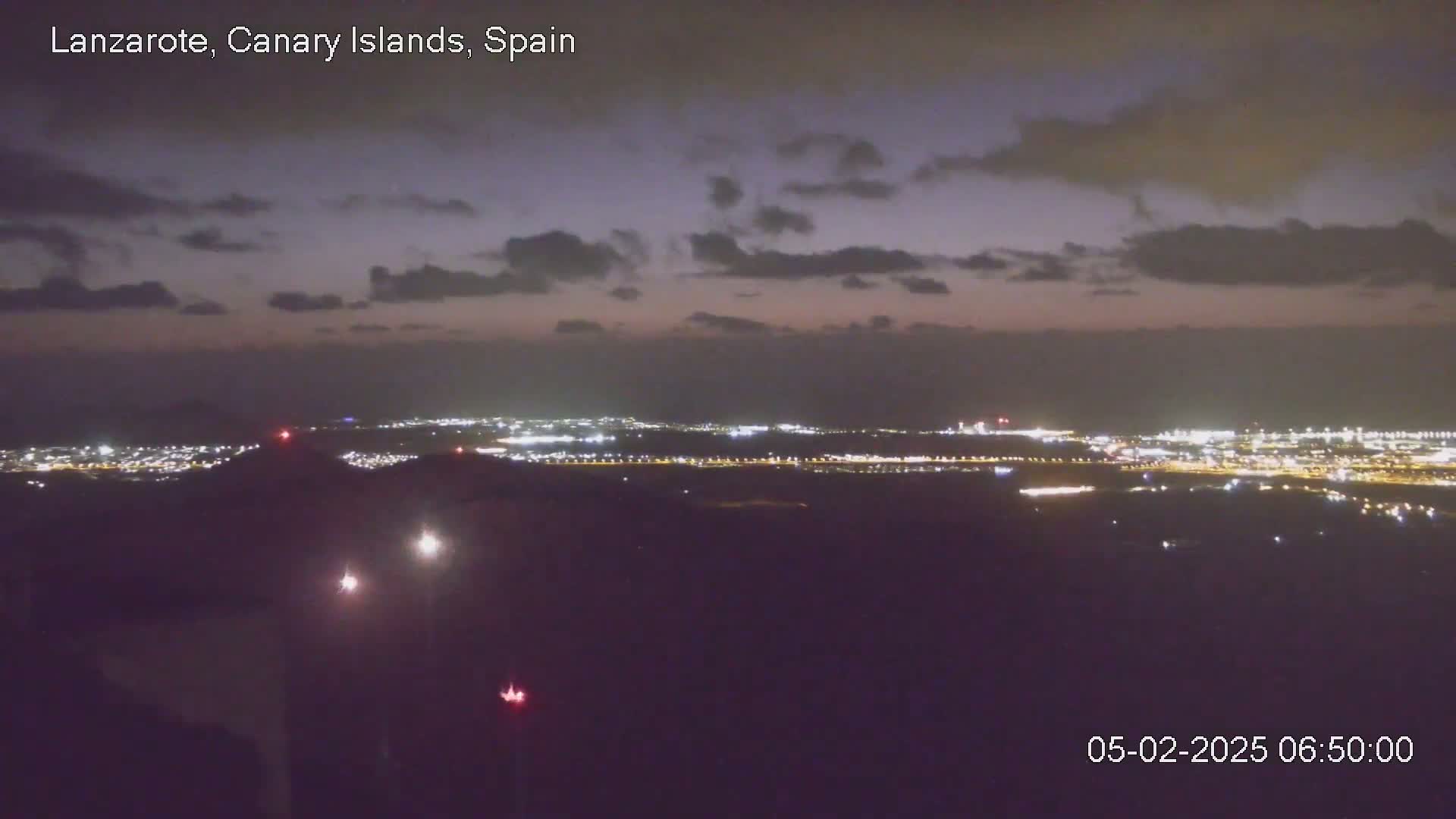 A nighttime view shows a sprawling city illuminated below a partly cloudy sky.