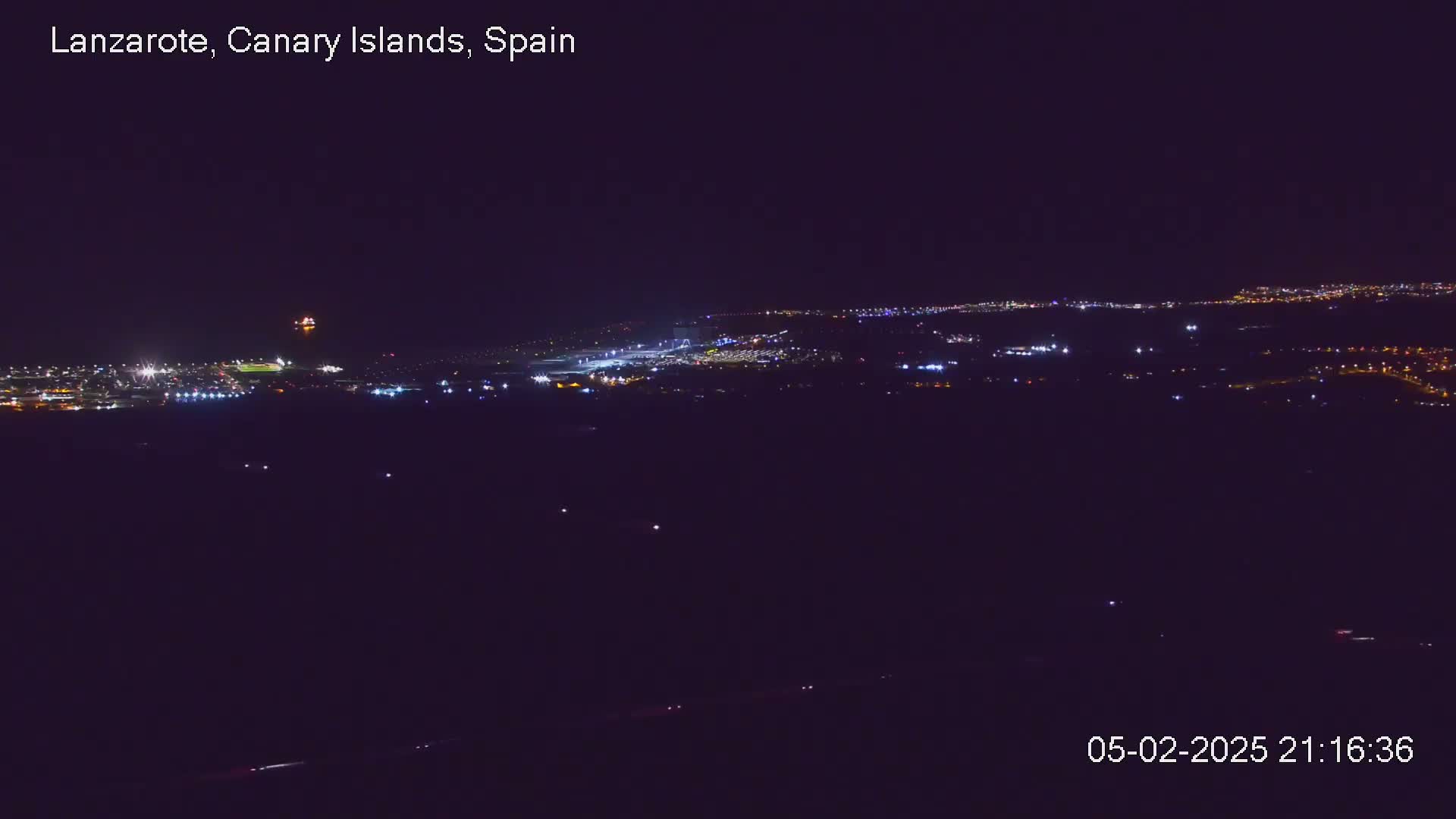 A nighttime long shot of a city's lights spread across a dark landscape under a clear sky.