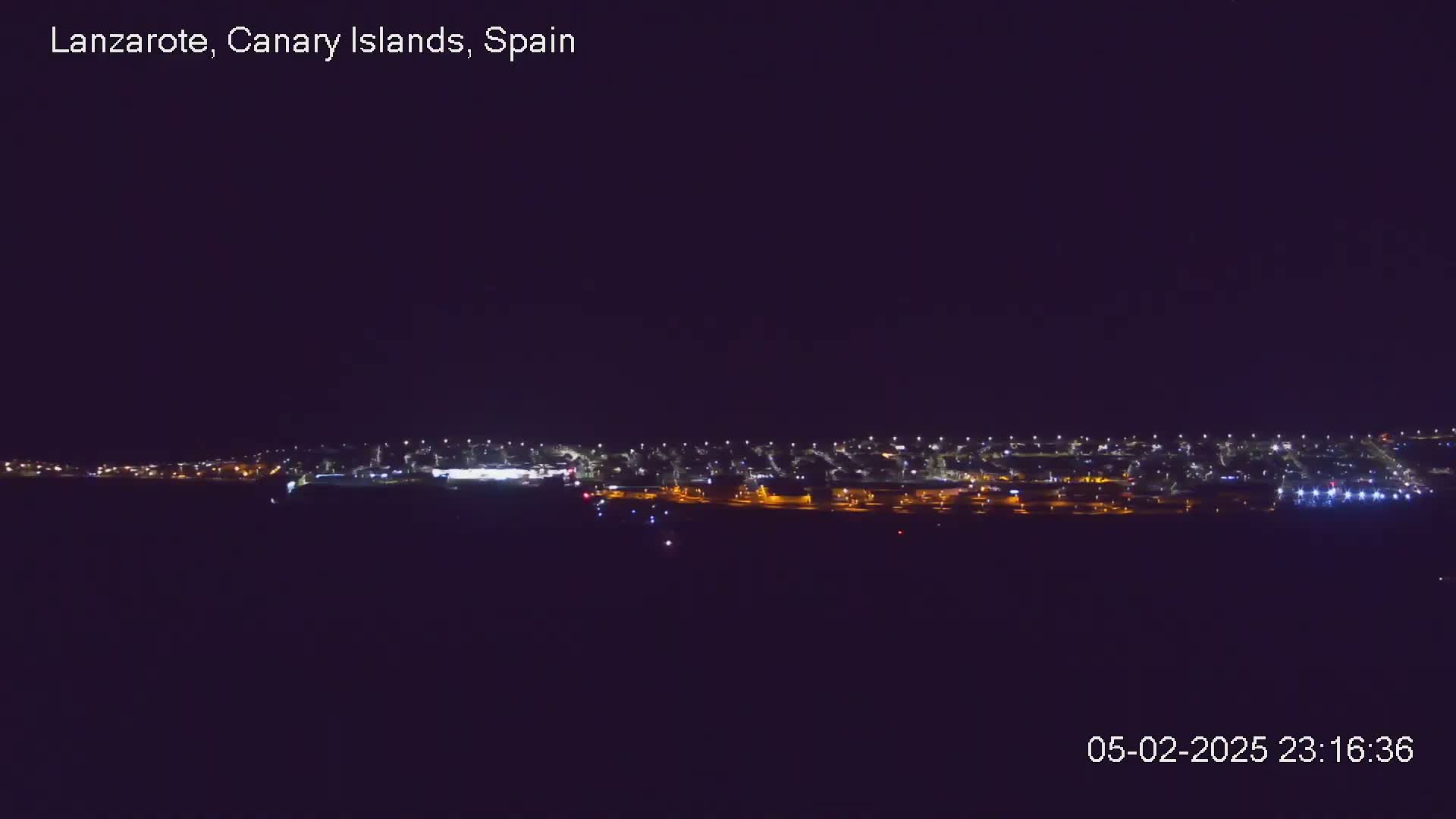 A nighttime long shot shows a string of city lights stretching across the horizon under a clear, dark sky.