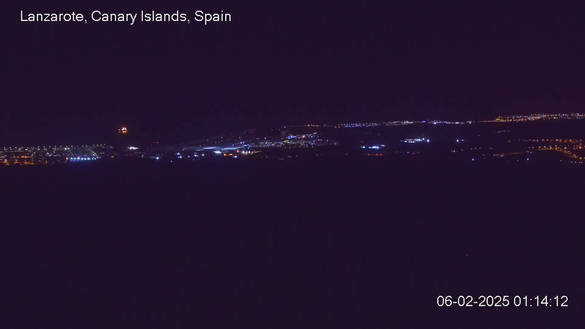 A nighttime long shot shows an airport with its runway lights illuminated against a dark sky.