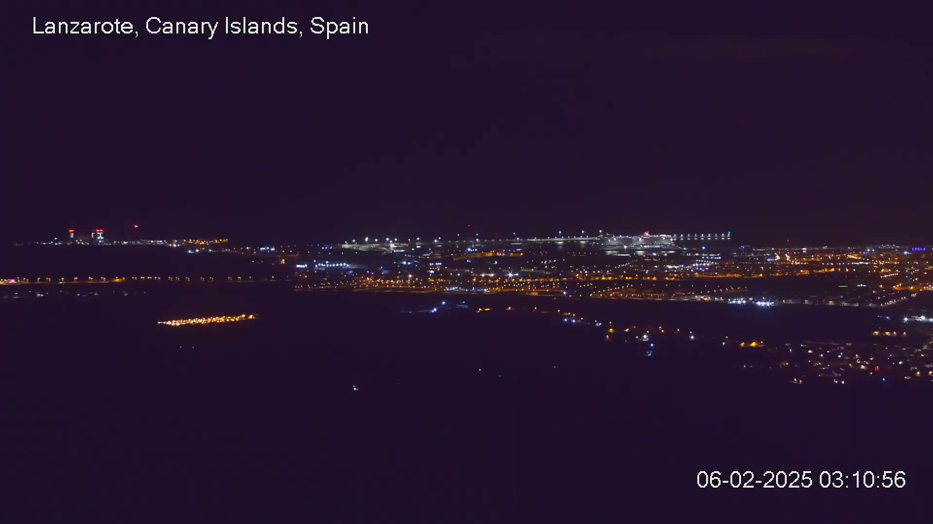 A nighttime long shot shows a city illuminated by many small lights, under a clear, dark sky.
