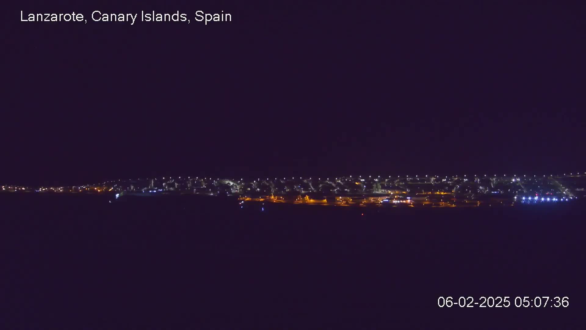 A nighttime long shot reveals a line of city lights stretching across the horizon under a dark, clear sky.