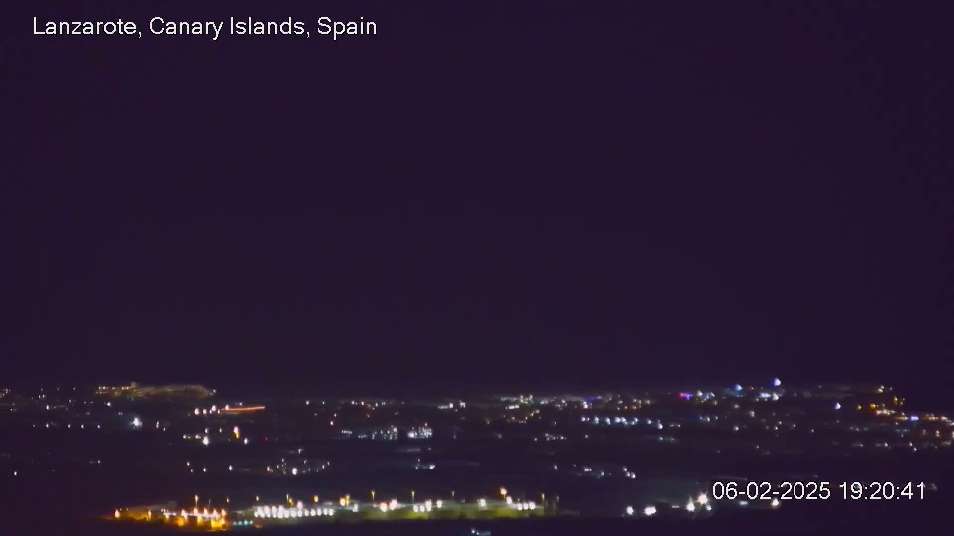 A nighttime, long-range view of a city illuminated by many scattered lights under a dark, clear sky.
