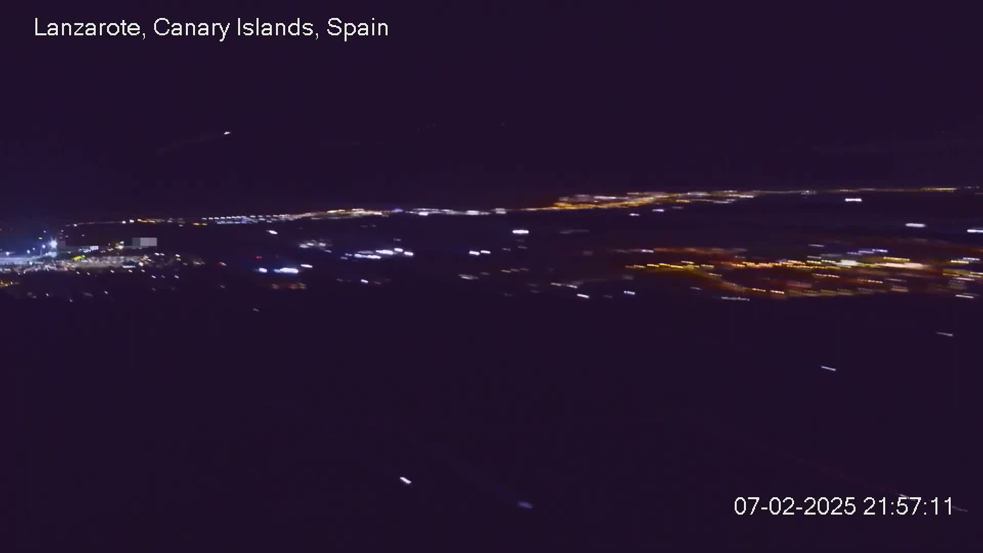 A nighttime, high-angle view shows a sprawling city's lights spread across a dark landscape.