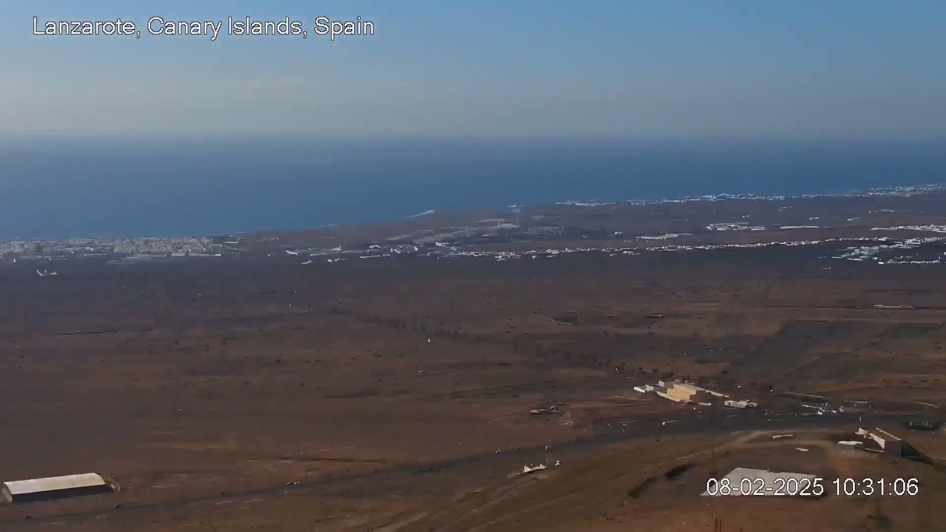 A vast, arid landscape stretches to a distant coastline and ocean under a clear, bright sky.
