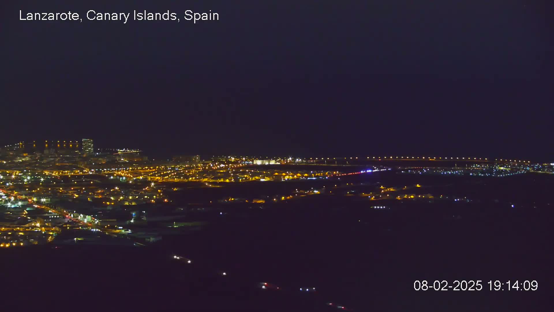 A nighttime, aerial view shows a city illuminated by numerous lights under a dark sky.