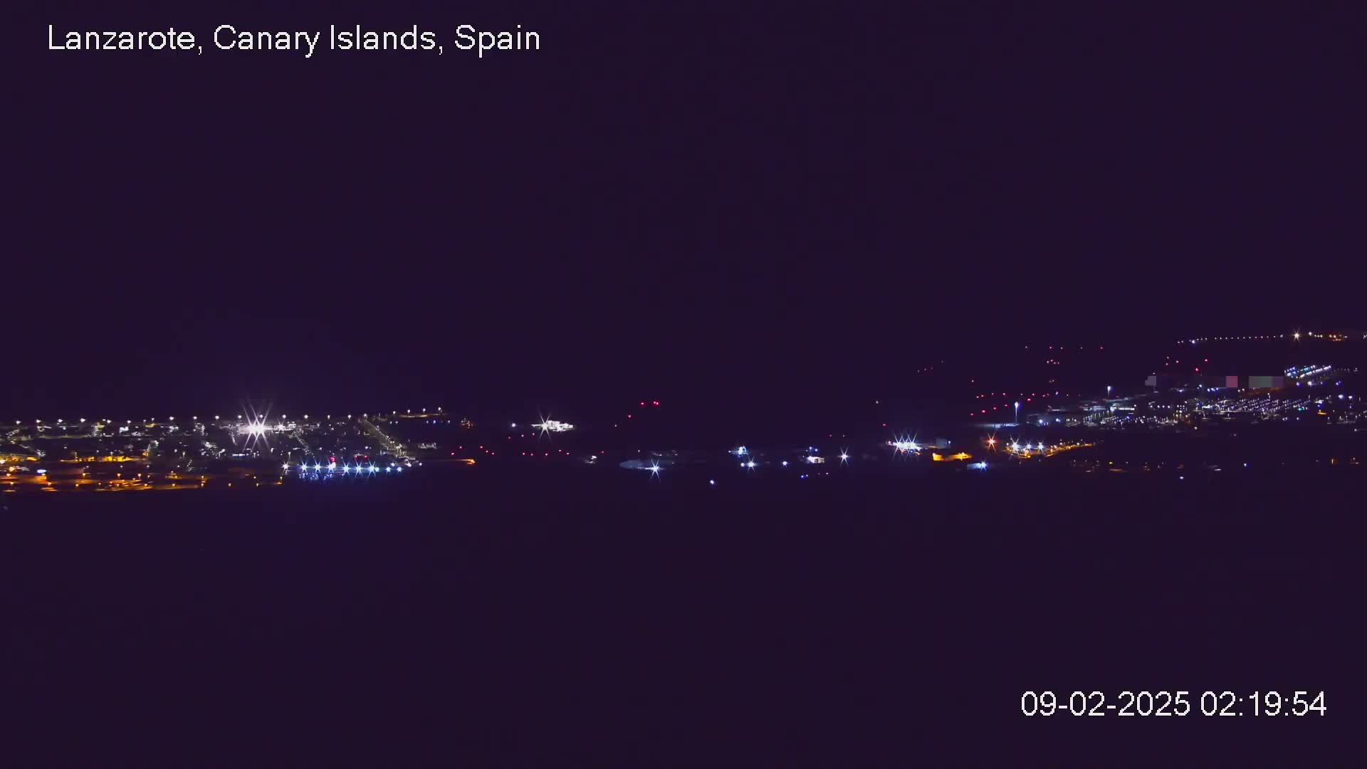 A nighttime long shot shows an airport illuminated with many lights under a clear, dark sky.