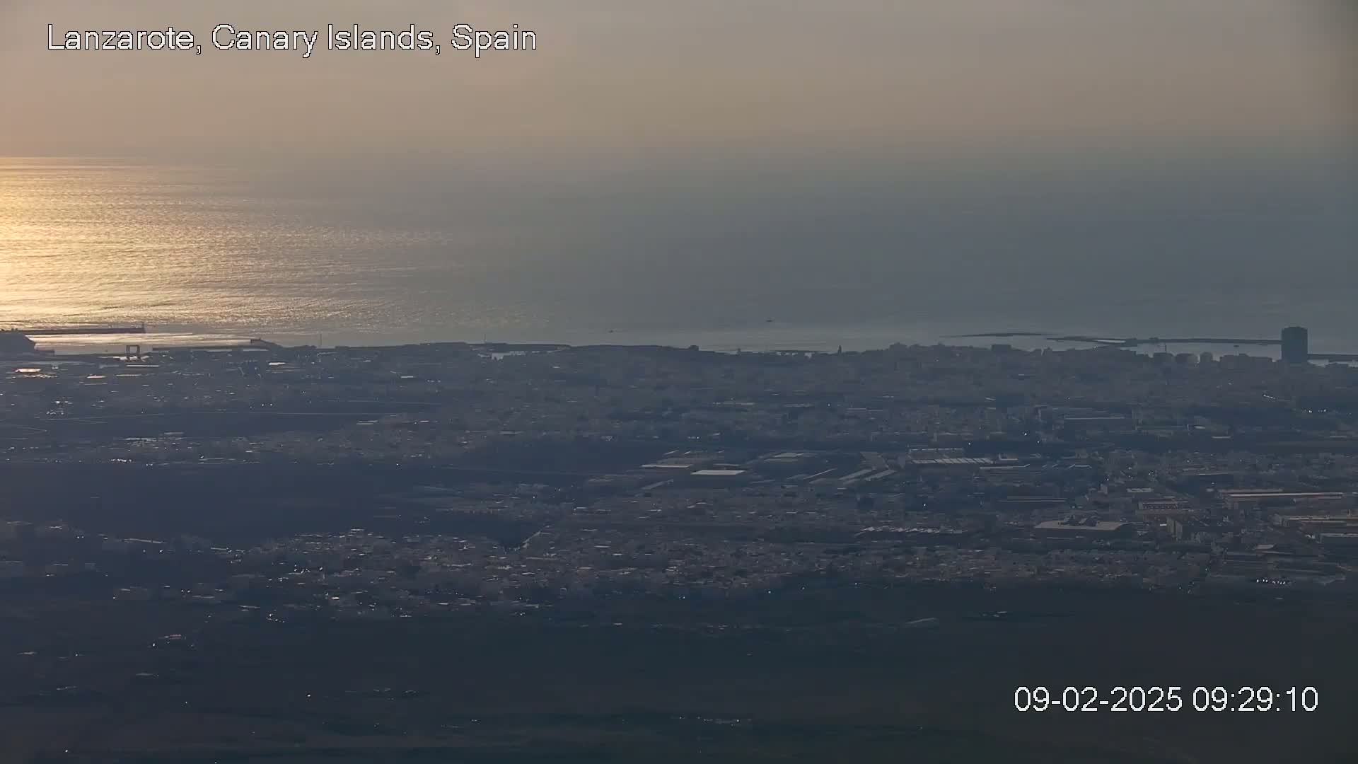 A hazy sunset illuminates a coastal city and ocean viewed from a high vantage point.