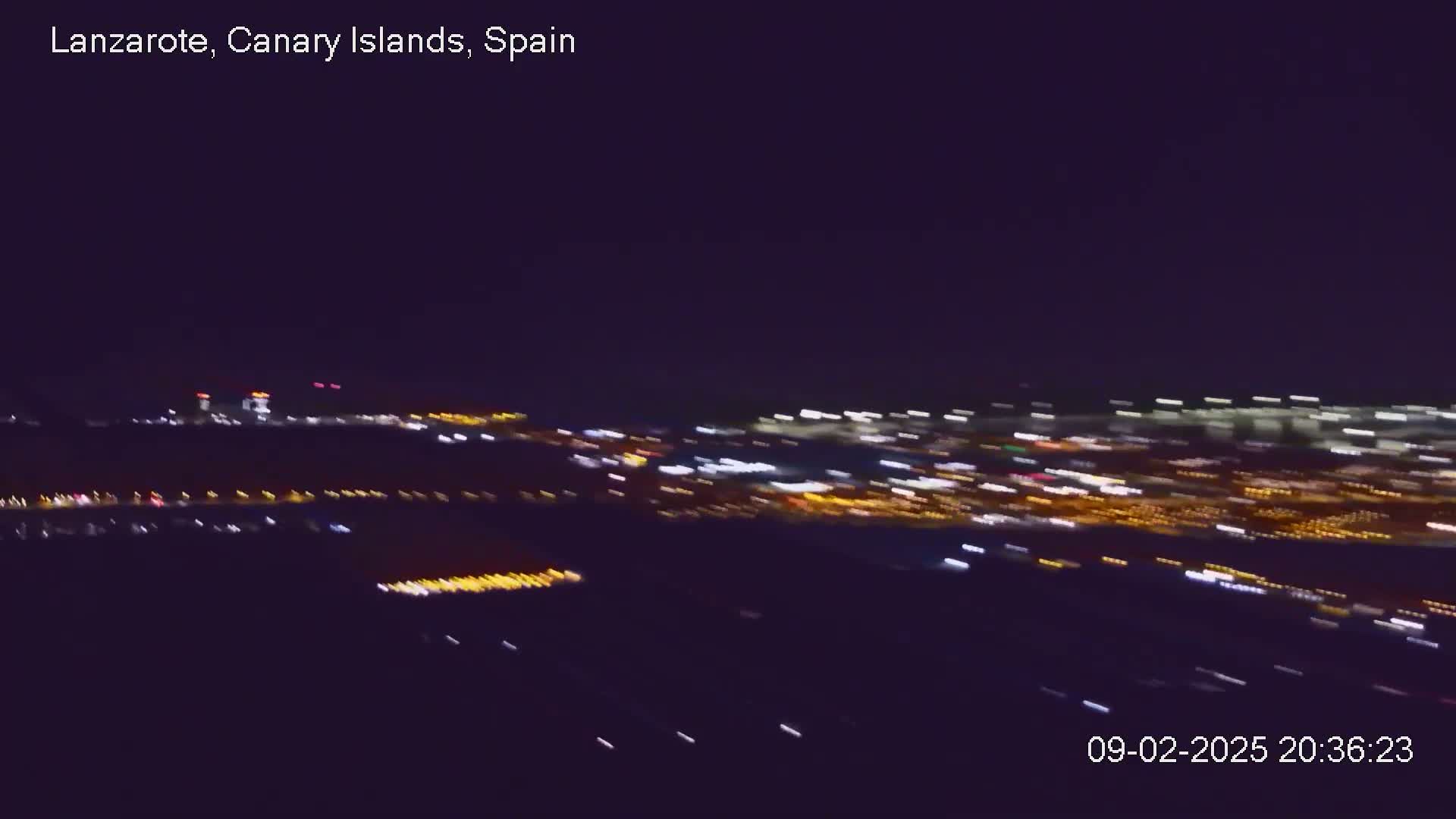 A blurry, nighttime aerial view shows a city's lights spread across the landscape.