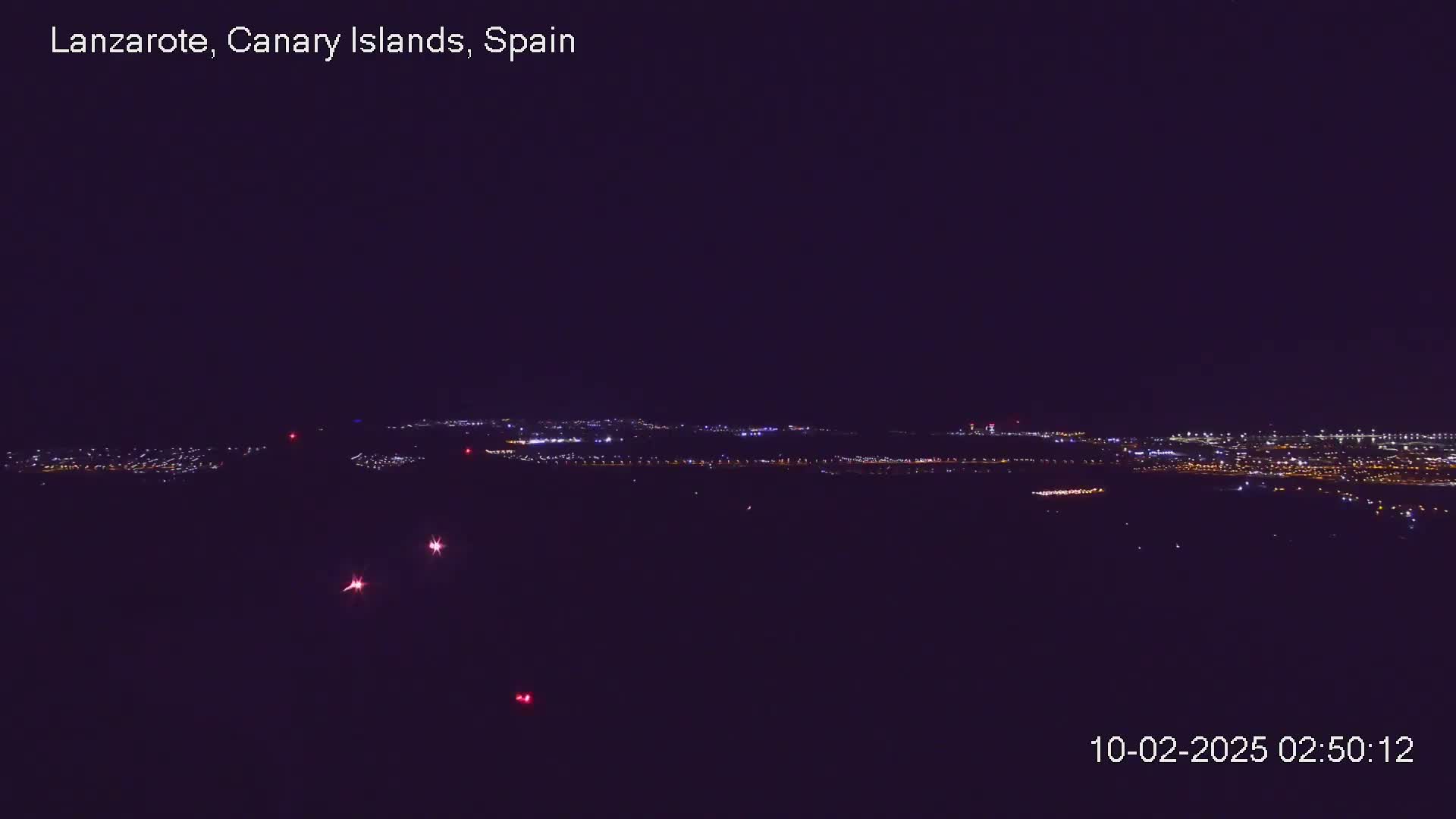 A nighttime long shot shows a distant city illuminated with many small lights under a clear, dark sky.