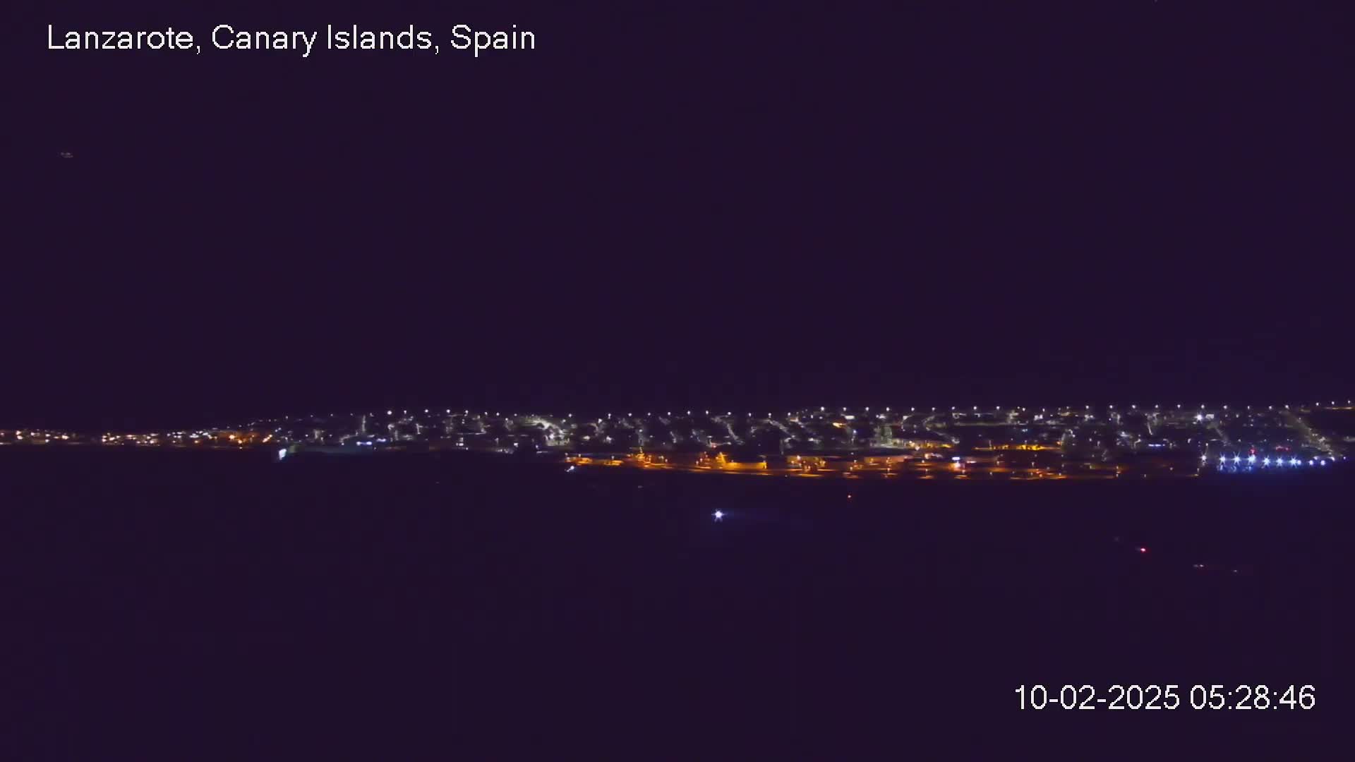 A nighttime long shot shows a city's lights spread across a dark landscape under a clear, dark sky.