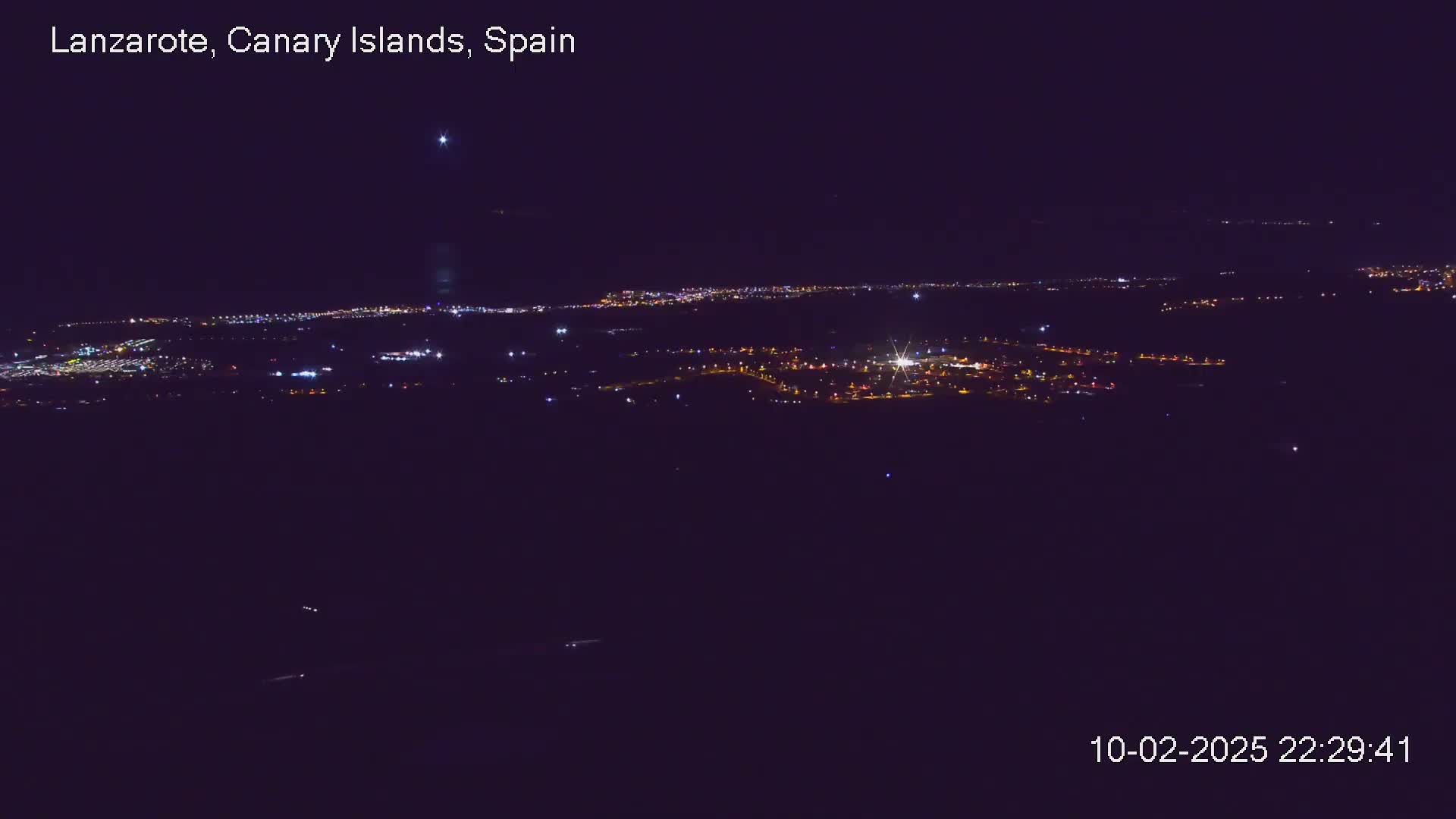 A nighttime, long-range view of a city's lights spread across a dark landscape under a clear sky.