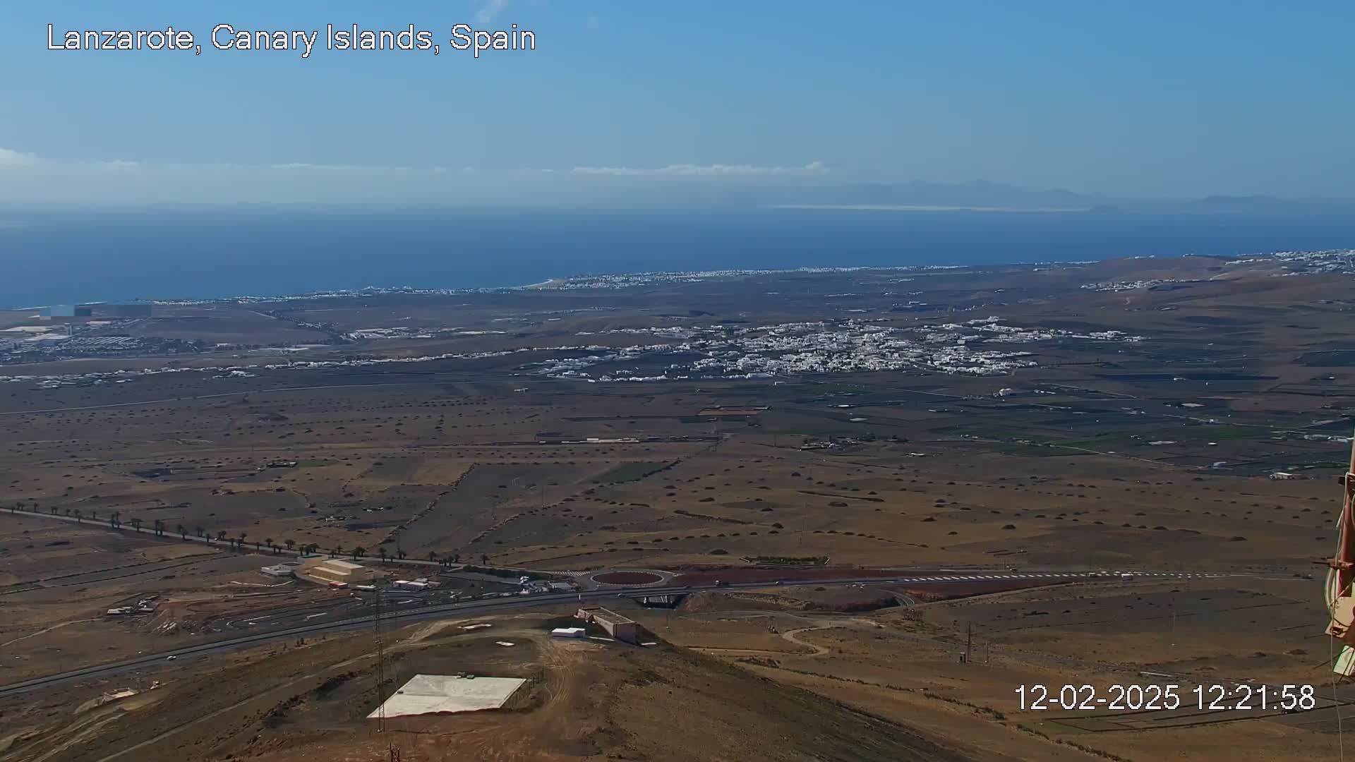 A high-angle, long shot on a clear day shows a coastal town, arid landscape, and ocean under a mostly clear sky.