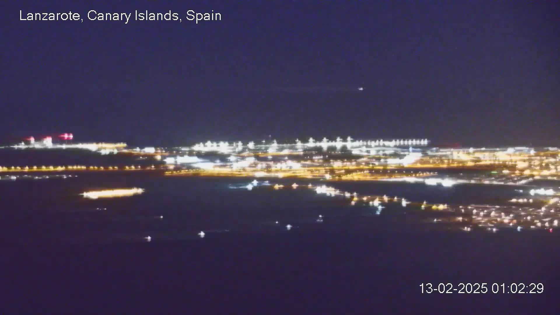 A nighttime, long-range view shows a city's lights spread across the landscape and reflected on dark water.