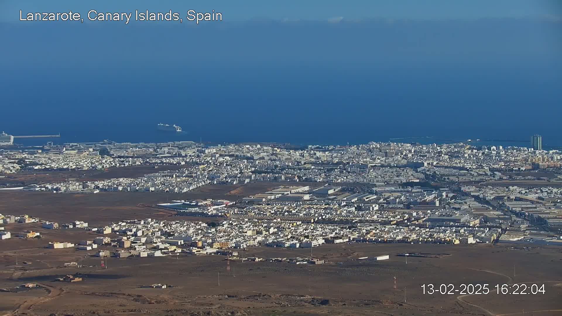 An expansive view of a coastal city on a clear, sunny day, with a large body of water visible in the background.