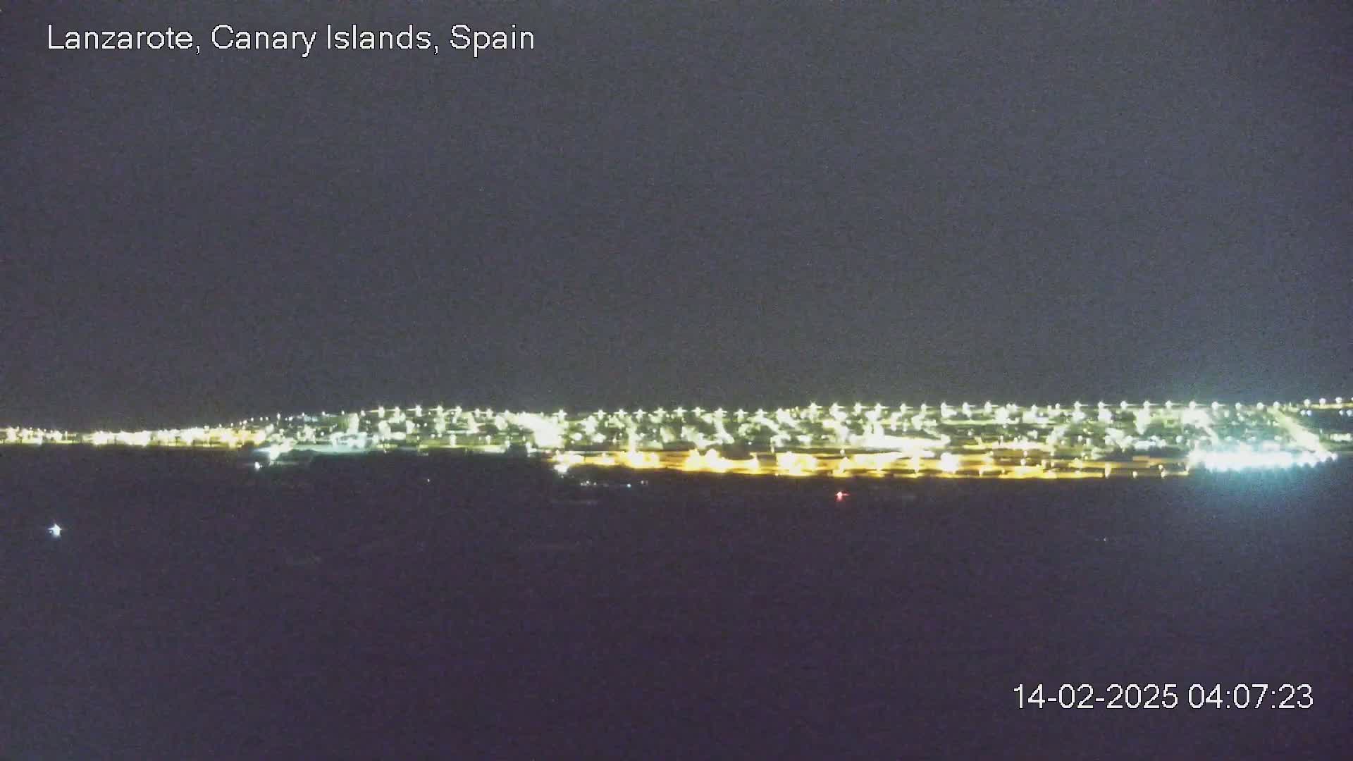 A long line of city lights stretches across the horizon at night under a dark, clear sky.