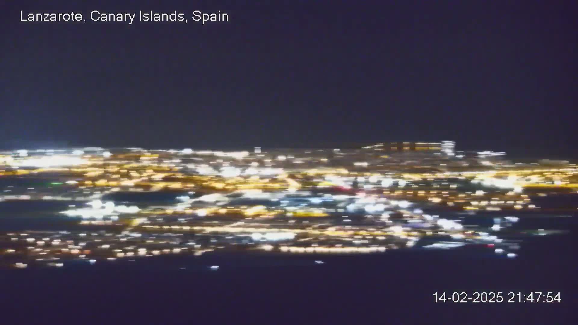 A blurry, nighttime aerial view shows a city illuminated by many lights under a dark sky.