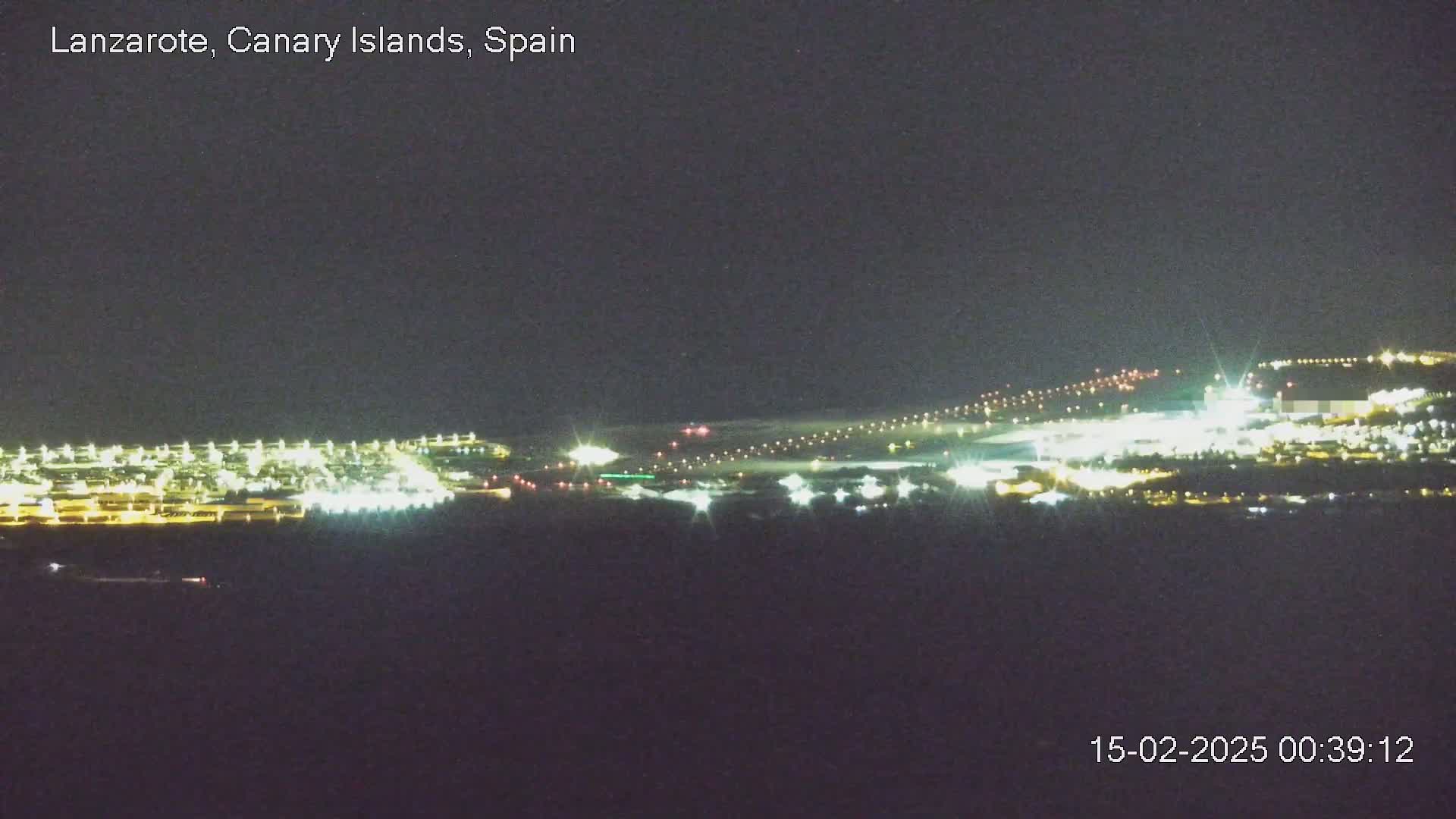 A brightly lit airport at night is visible from a distance under a dark, clear sky.