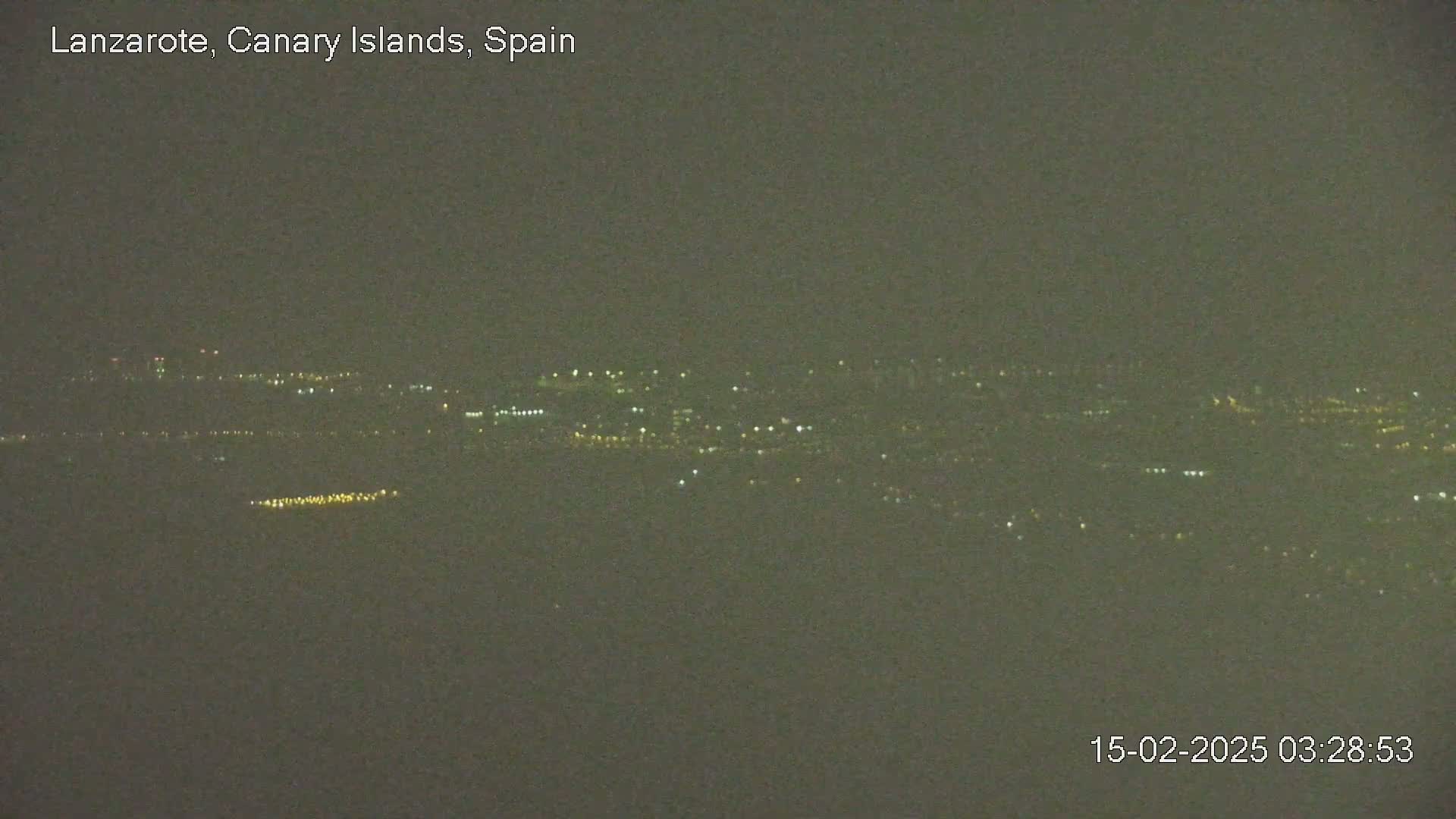 A hazy, dark night view shows distant city lights spread across a landscape.