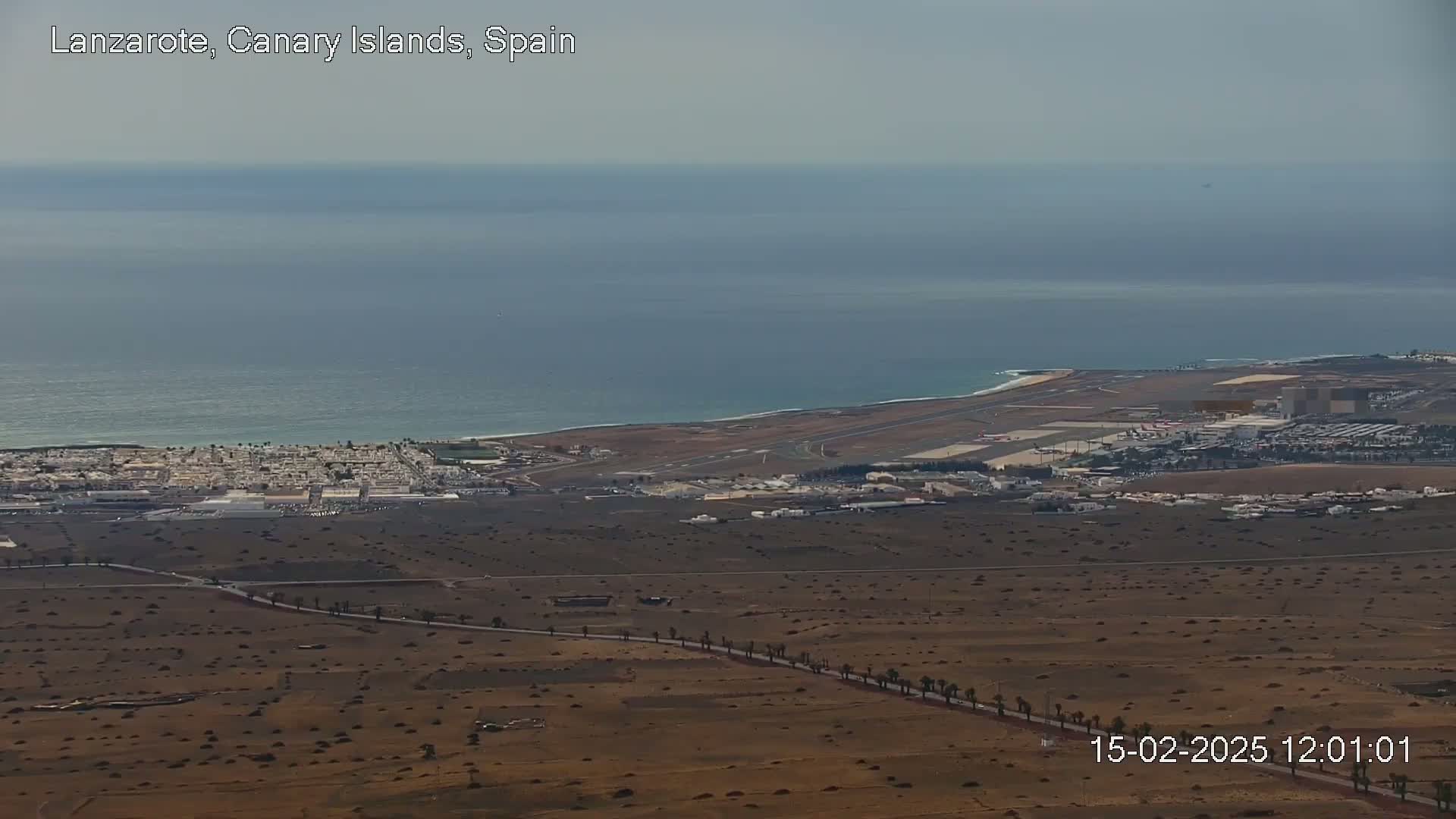 A coastal airport and town are visible on a hazy day, with a calm ocean stretching to the horizon.