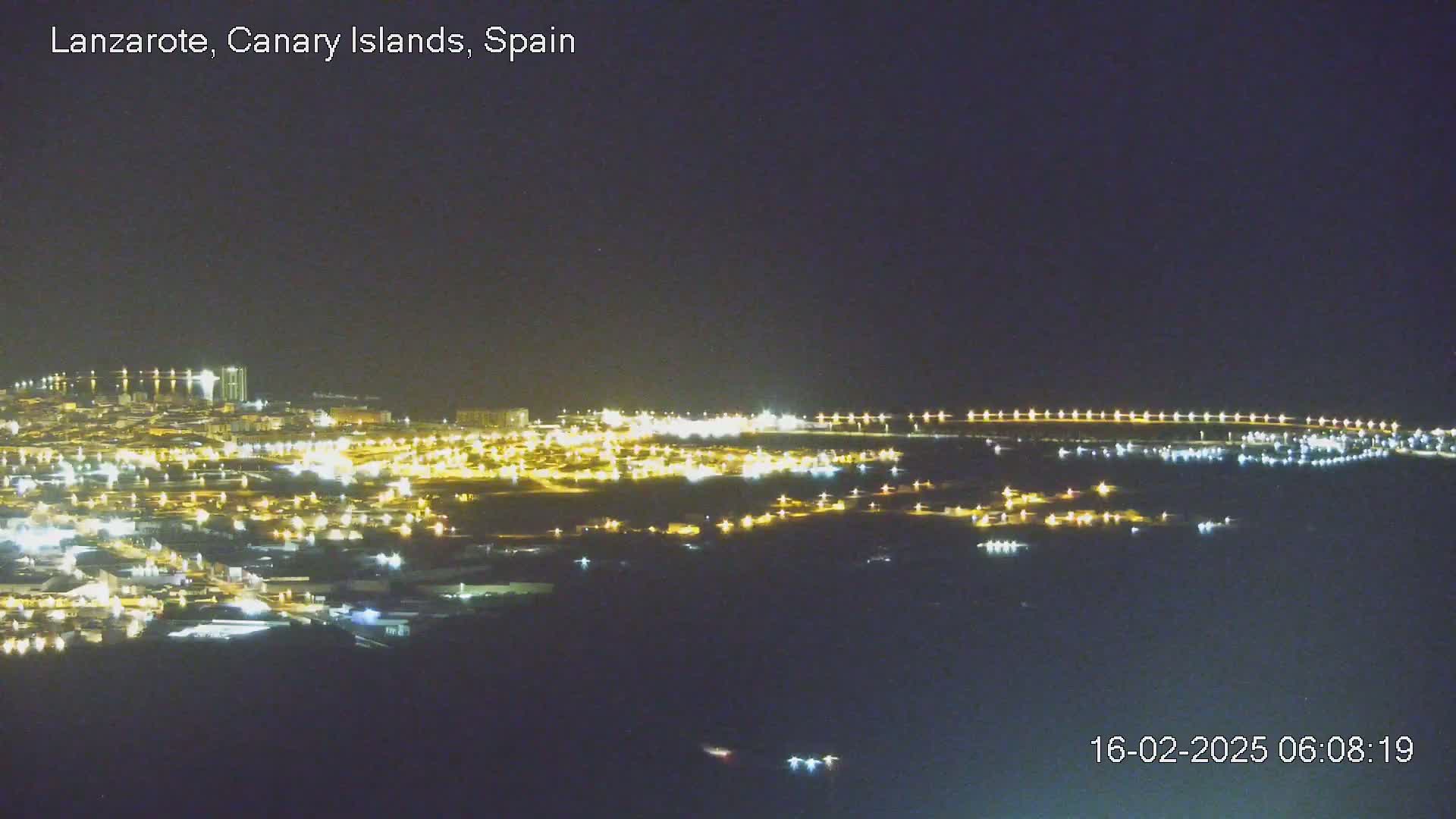 A nighttime aerial view of a coastal city illuminated by numerous lights, under a clear dark sky.