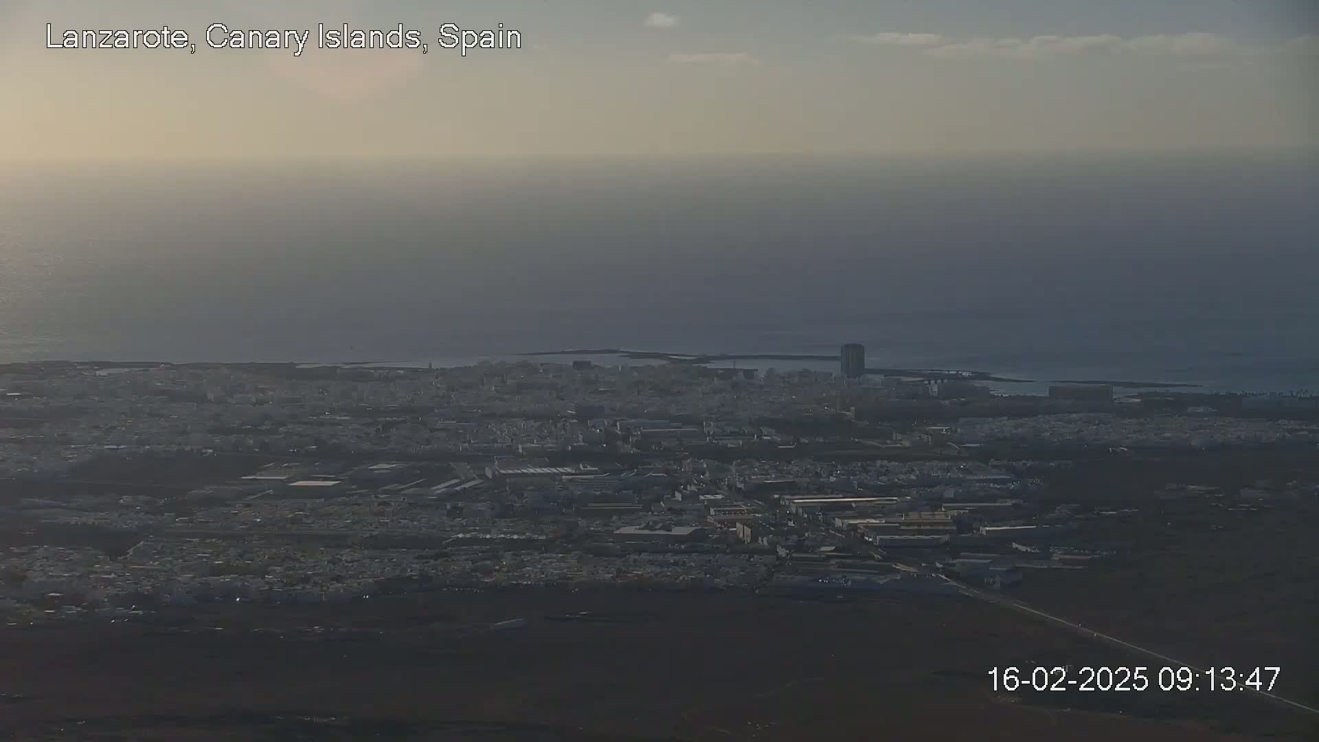 A hazy, overcast day reveals a sprawling coastal city, with a body of water visible in the background.