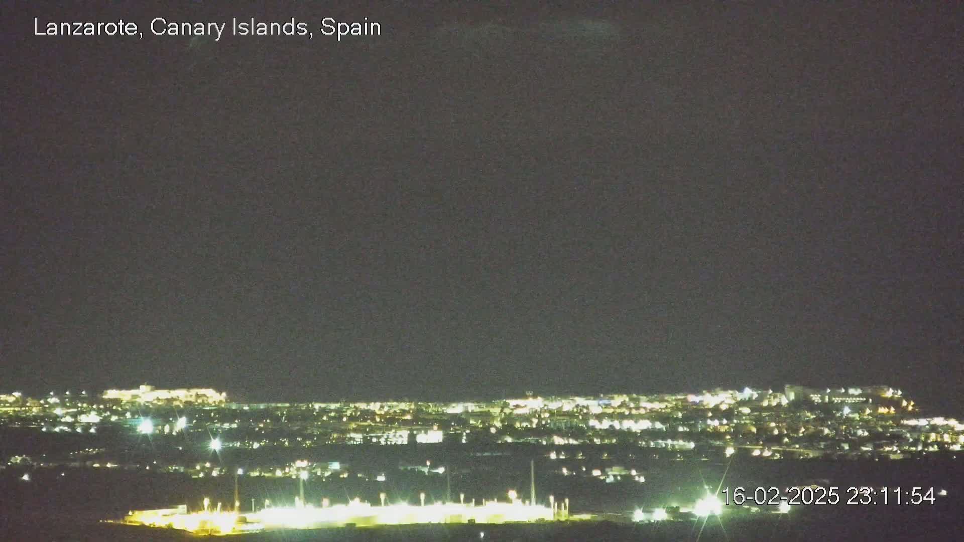 A nighttime long shot shows a city illuminated with lights under a dark, clear sky.