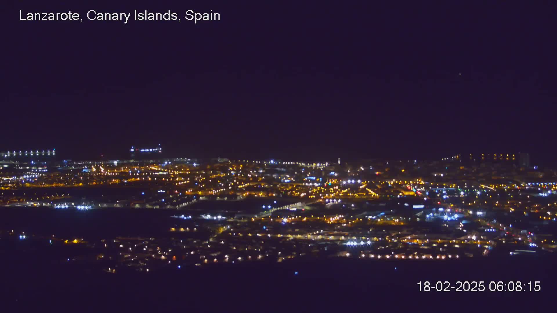 A sprawling city at night is illuminated by countless lights under a clear, dark sky.