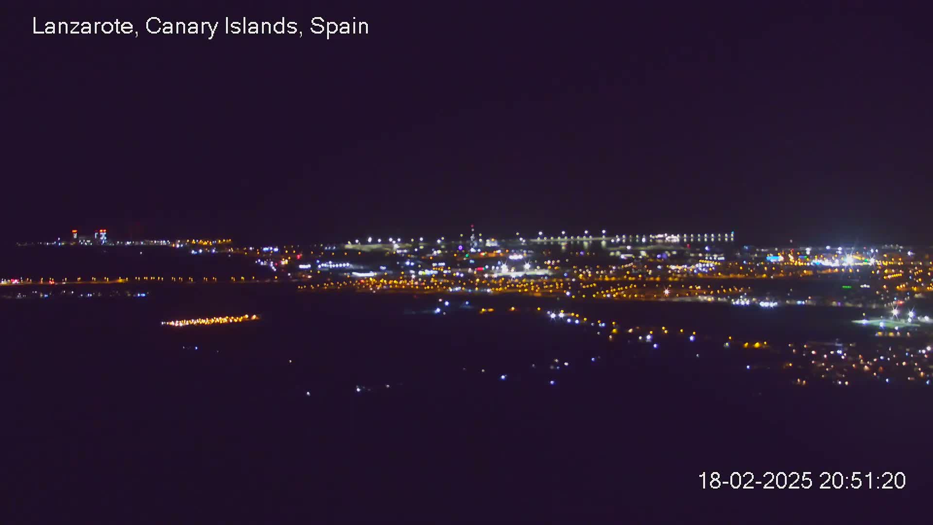 A nighttime long shot shows a city illuminated by many small, scattered lights under a clear, dark sky.