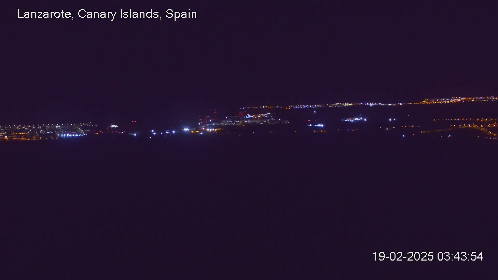 A nighttime long shot shows a city illuminated by scattered lights under a clear, dark sky.
