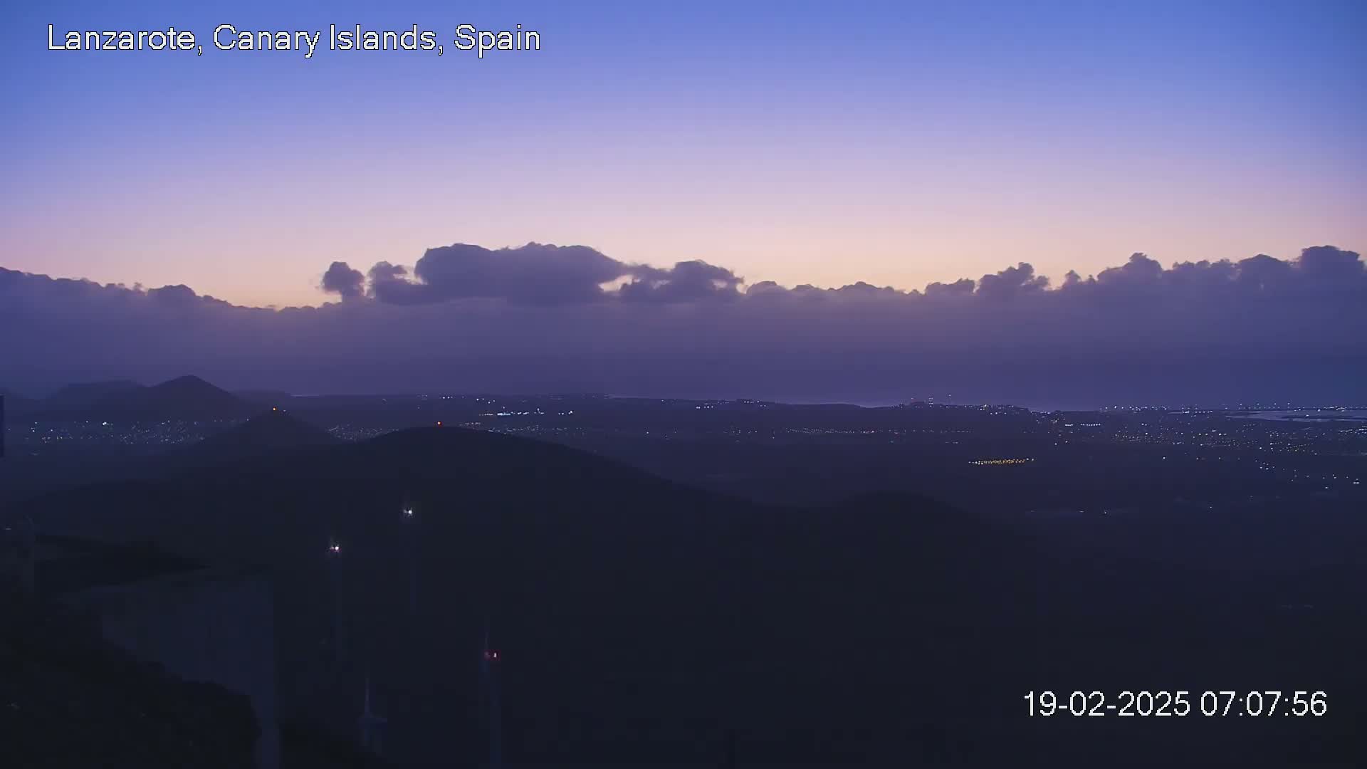 A twilight view shows a low-lying layer of clouds over a dark, hilly landscape dotted with faint lights.