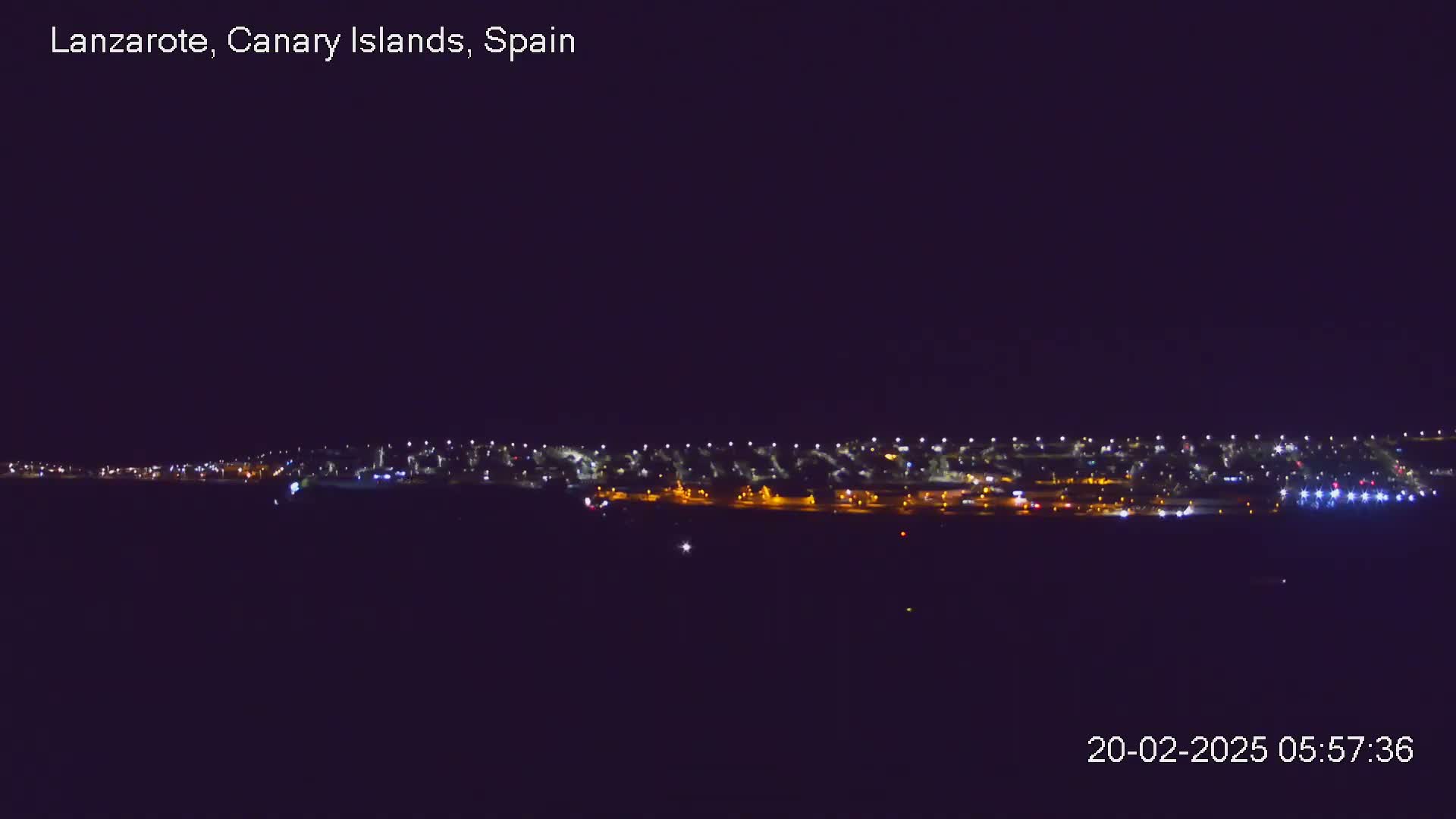 A long line of lights from a town or city is visible at night under a clear, dark sky.