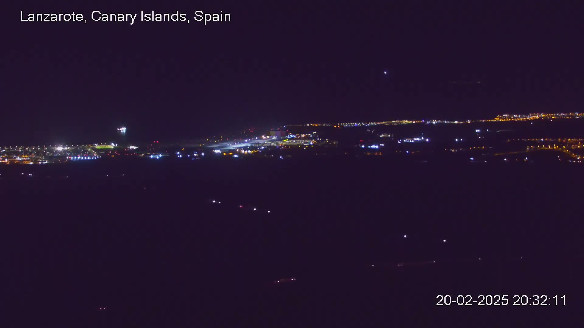 A nighttime, long-range view of an airport runway and surrounding city lights.