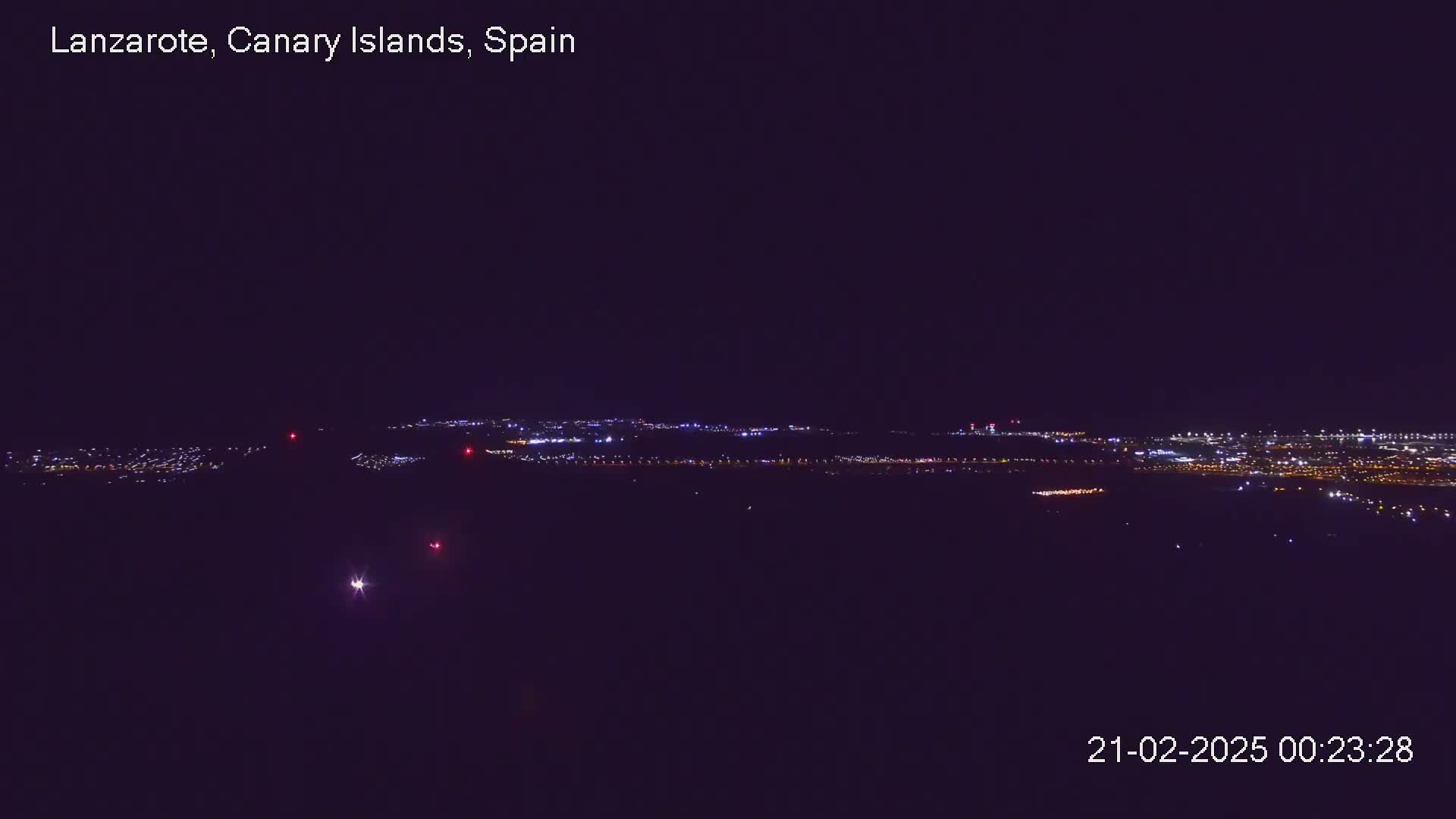 A nighttime long shot shows a city's lights spread across a dark landscape under a clear, dark sky.