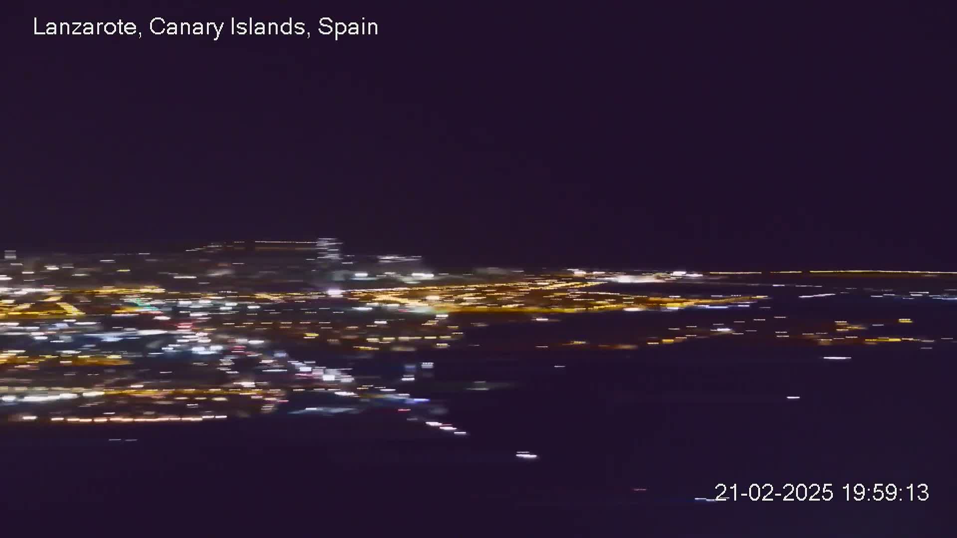 A nighttime aerial view shows a sprawling city illuminated by numerous lights under a clear, dark sky.