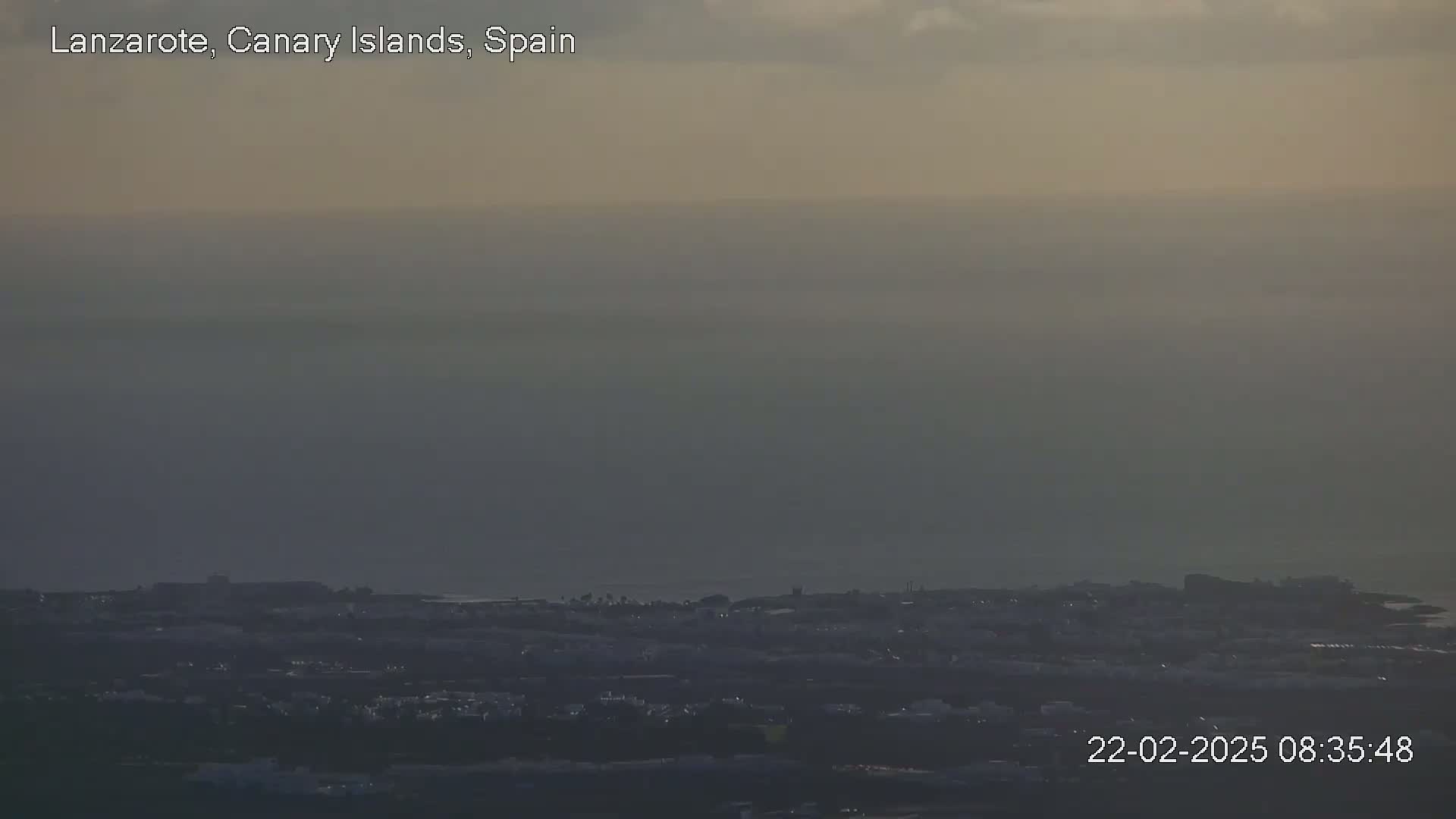 A hazy view of a coastal town stretches to a distant, obscured ocean under a muted sky.