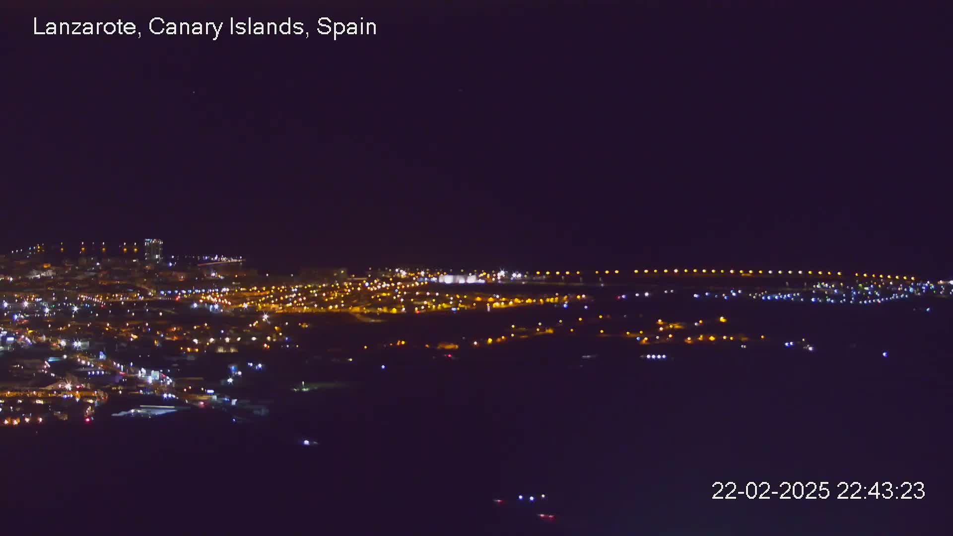 A nighttime long shot shows a city's lights spread across a dark landscape under a clear sky.