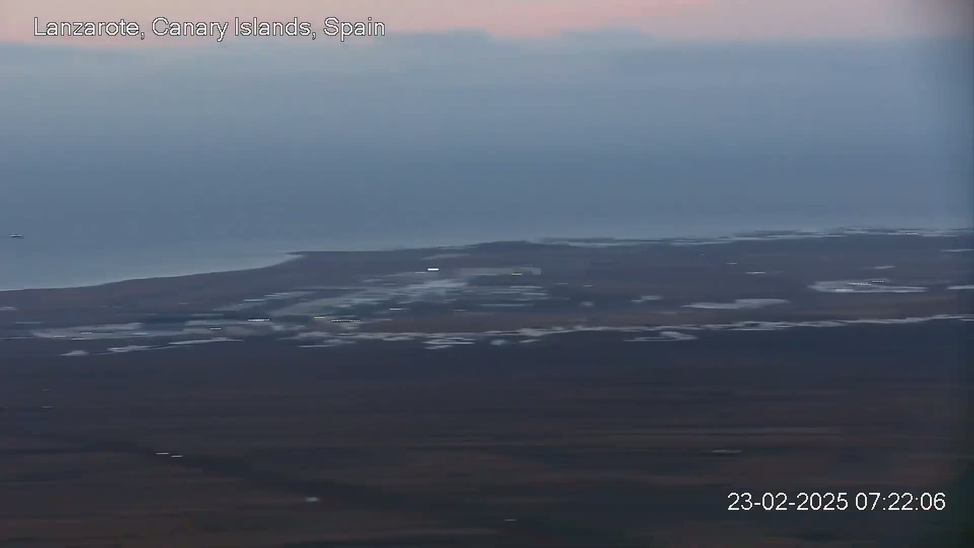 A hazy, dusky view shows a flat, dark landscape meeting a calm ocean under a pale sky.