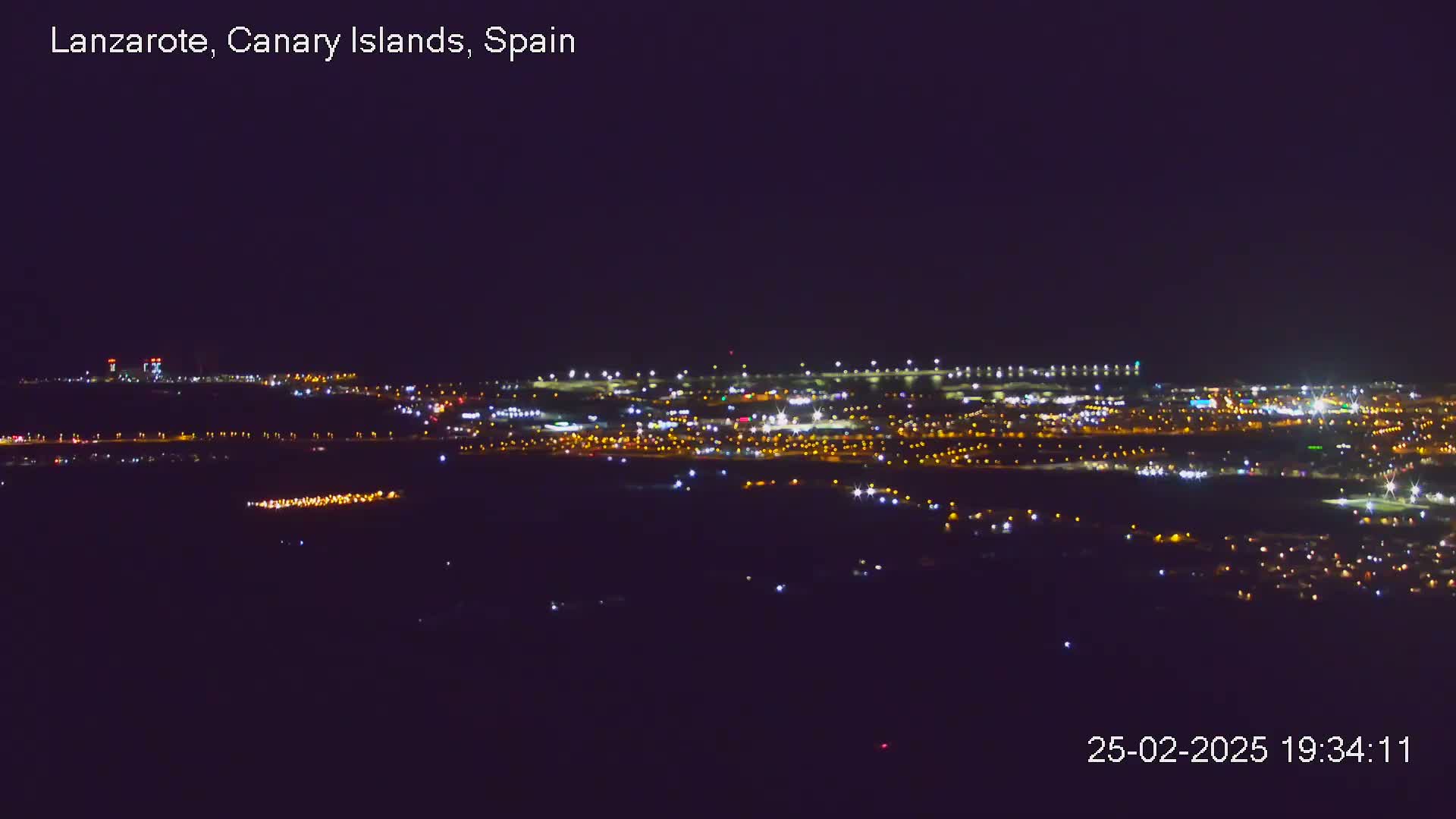 A nighttime, long-distance view of a city and airport illuminated by numerous lights under a clear, dark sky.