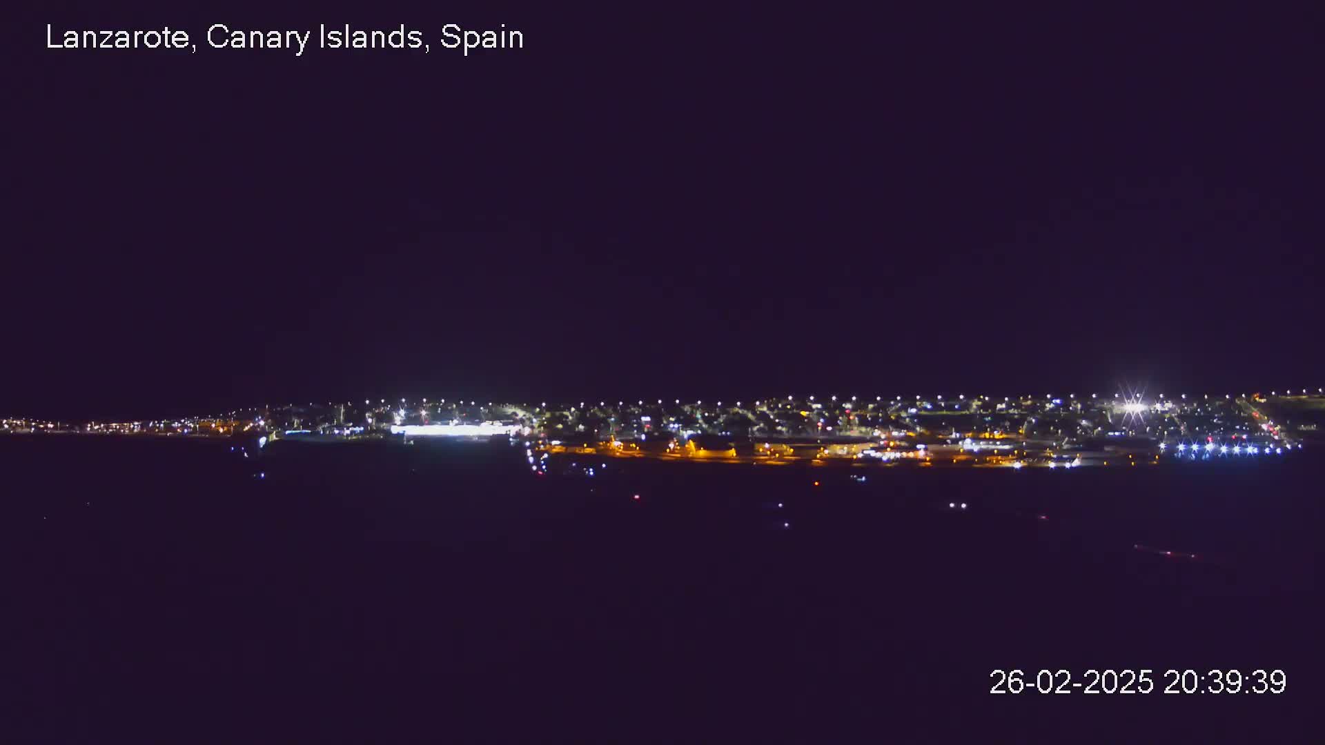 A nighttime long shot shows a city illuminated by many lights under a clear, dark sky.