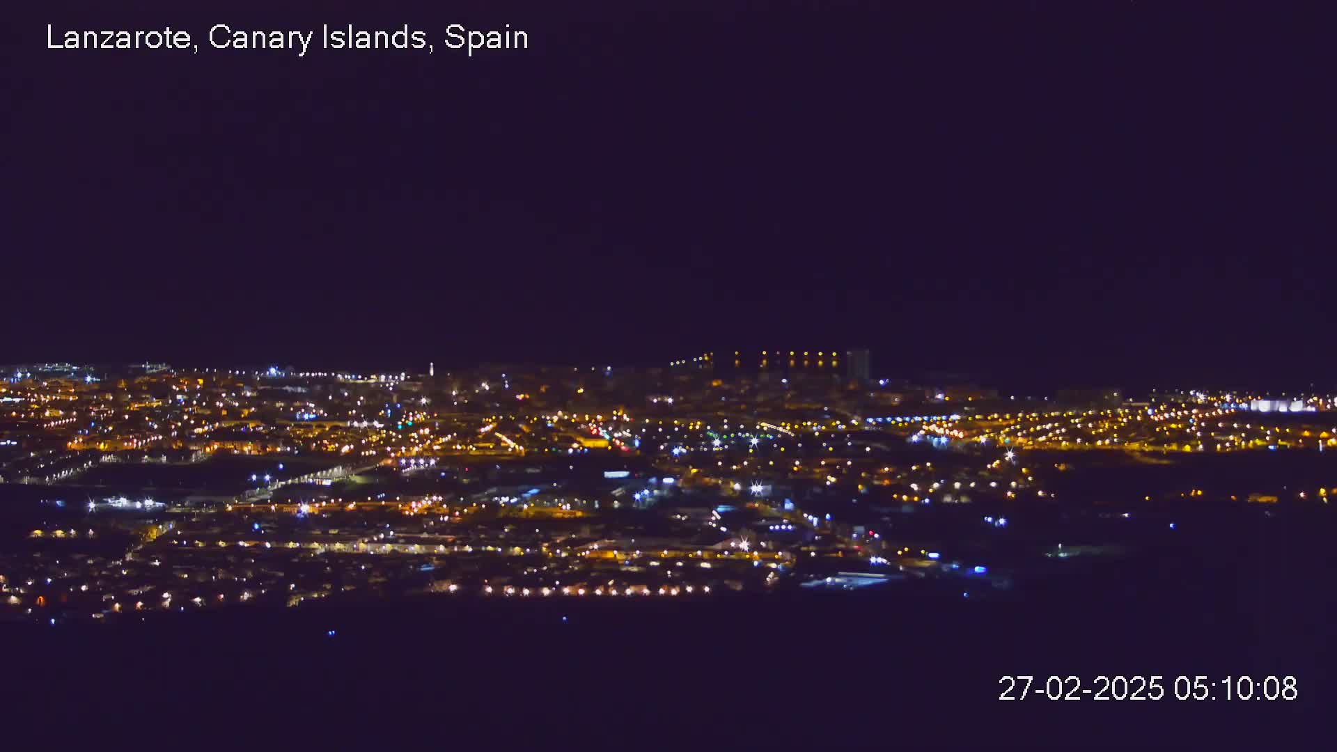A sprawling city at night is illuminated by countless lights under a clear, dark sky.