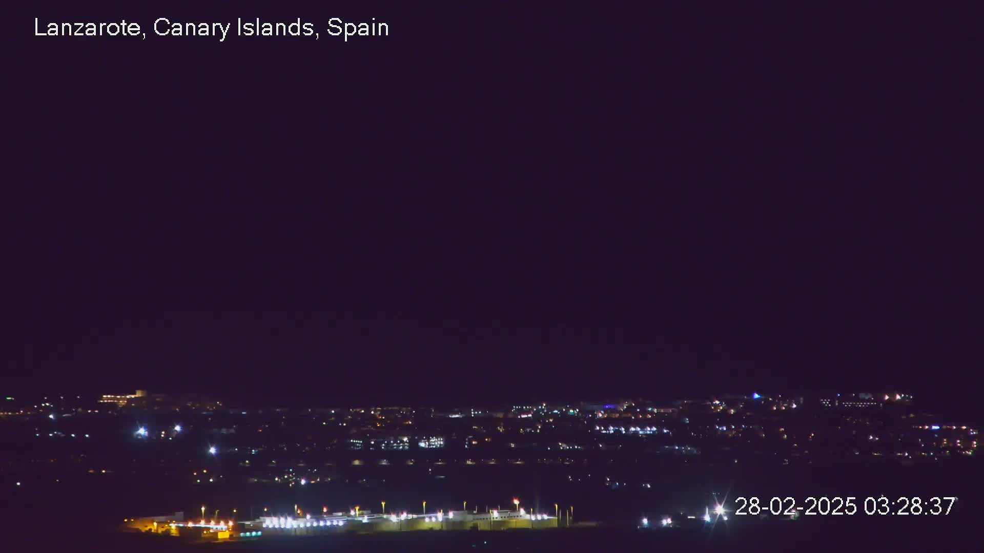 A nighttime view of a city with numerous lights, under a dark, clear sky.