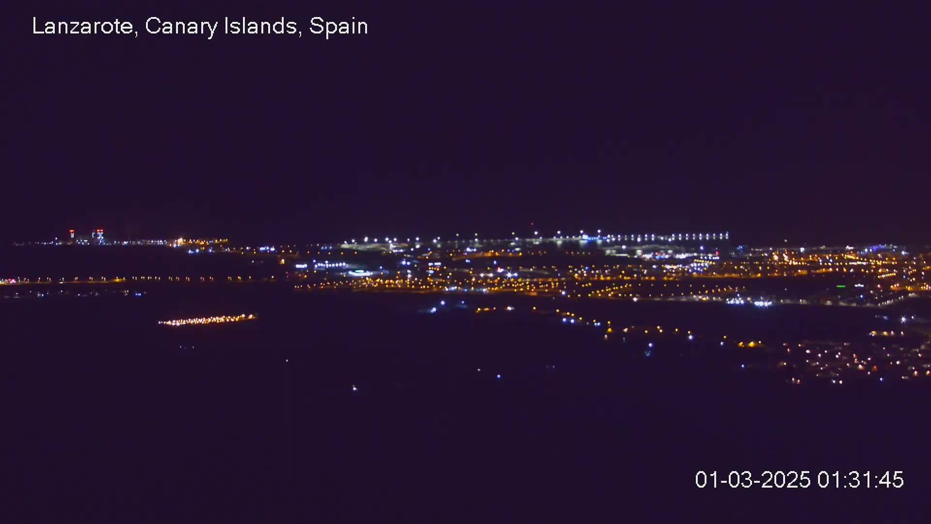 A nighttime, long-range view of a city illuminated by numerous lights, under a clear, dark sky.