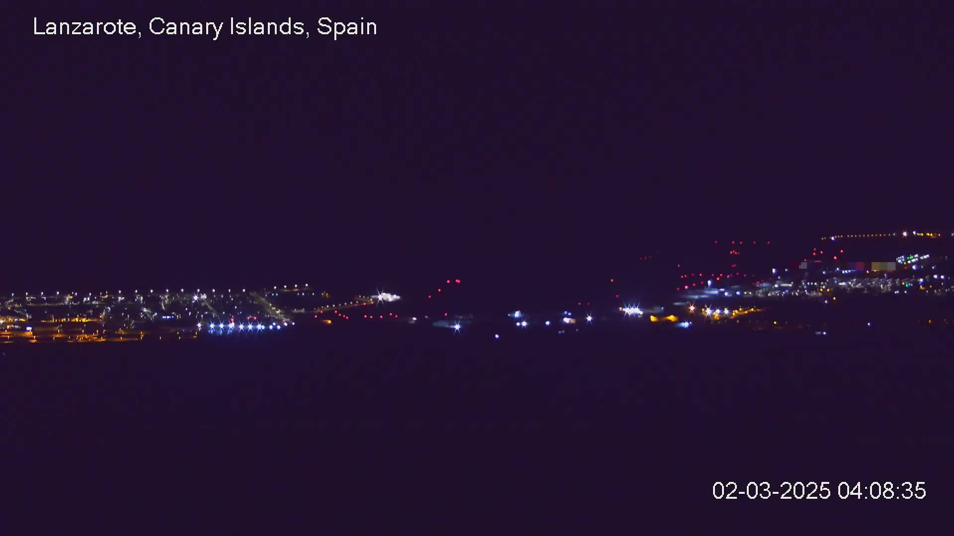A nighttime long shot shows a cluster of lights from a town or city under a clear, dark sky.