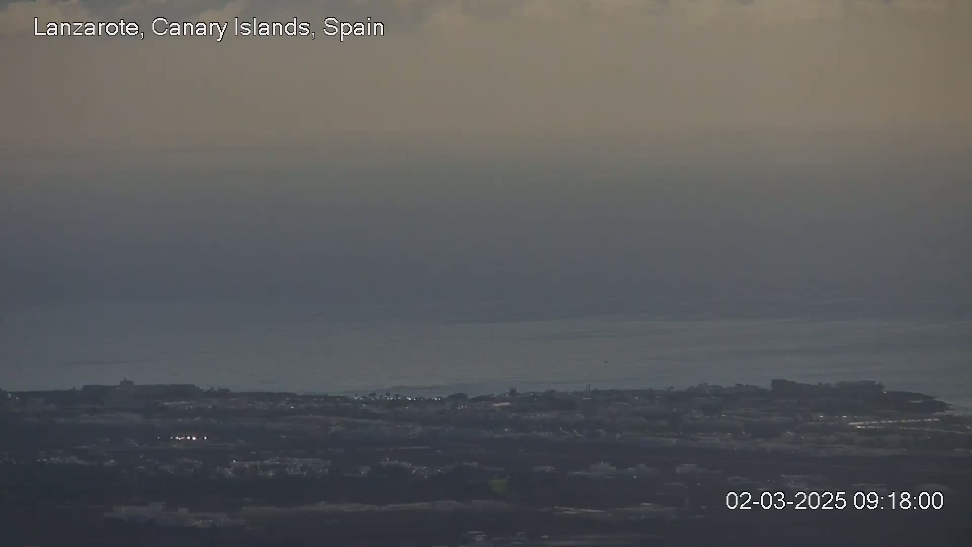 A hazy, overcast view shows a coastal town next to a calm ocean.