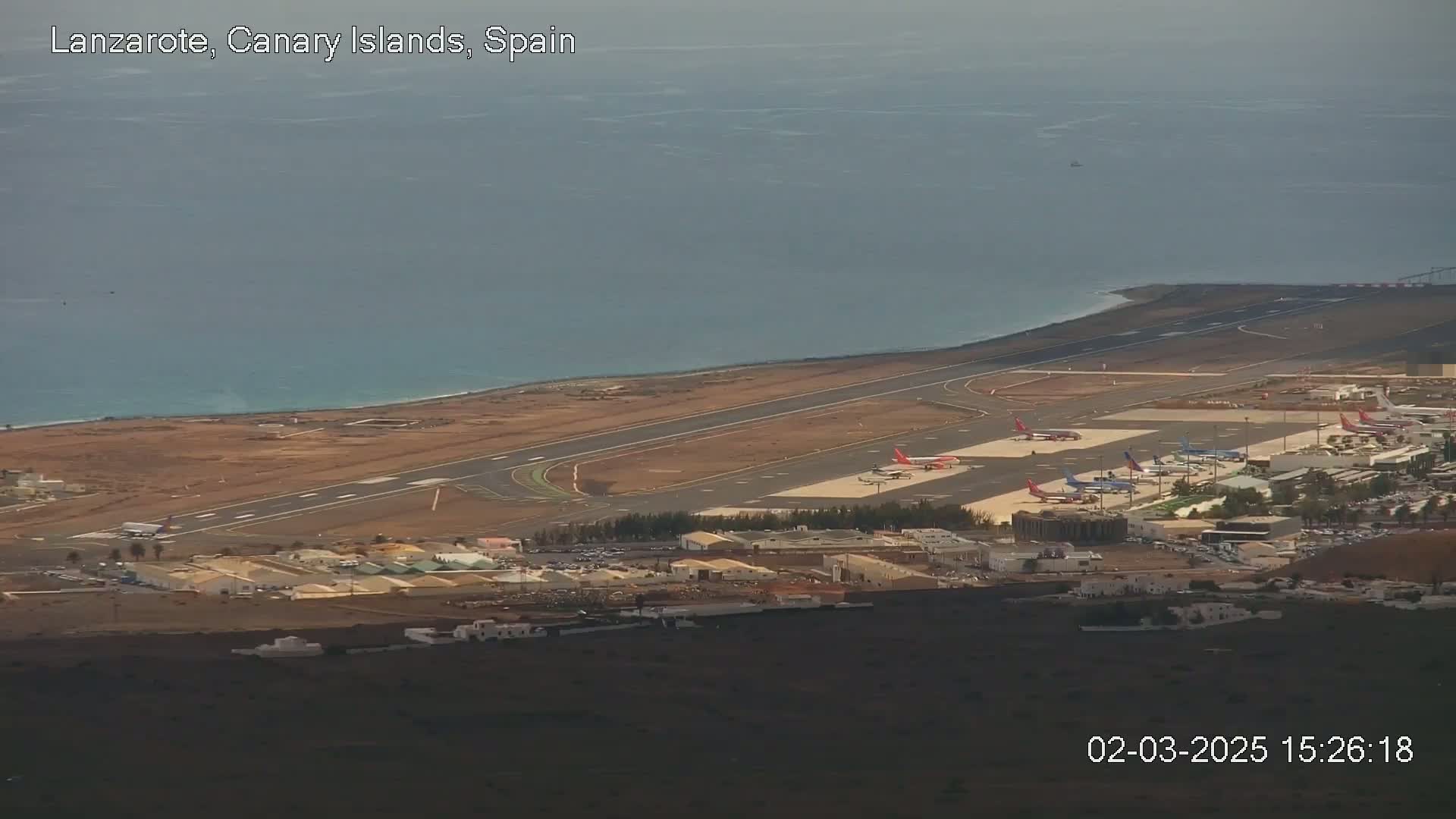 An airport with several airplanes on the tarmac sits beside a calm ocean under an overcast sky.