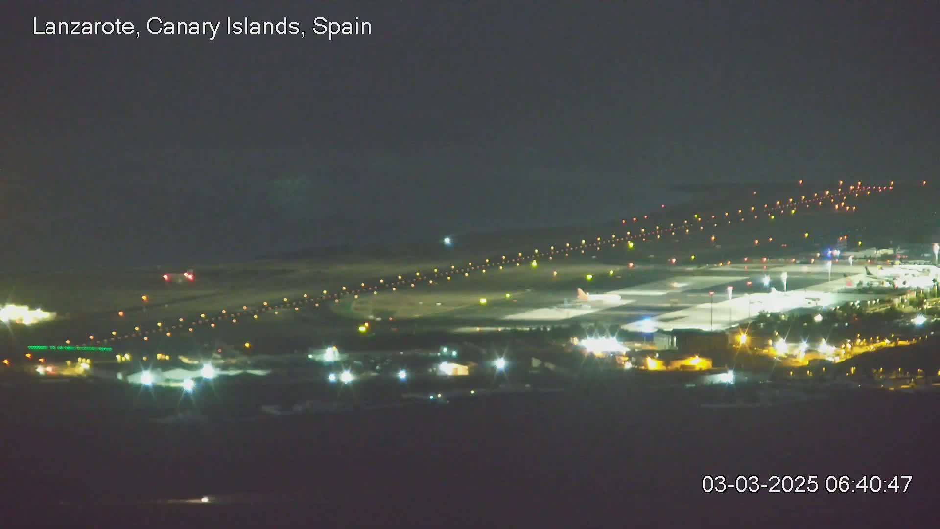 A brightly lit airport at night is shown, with planes on the tarmac and lights illuminating runways.