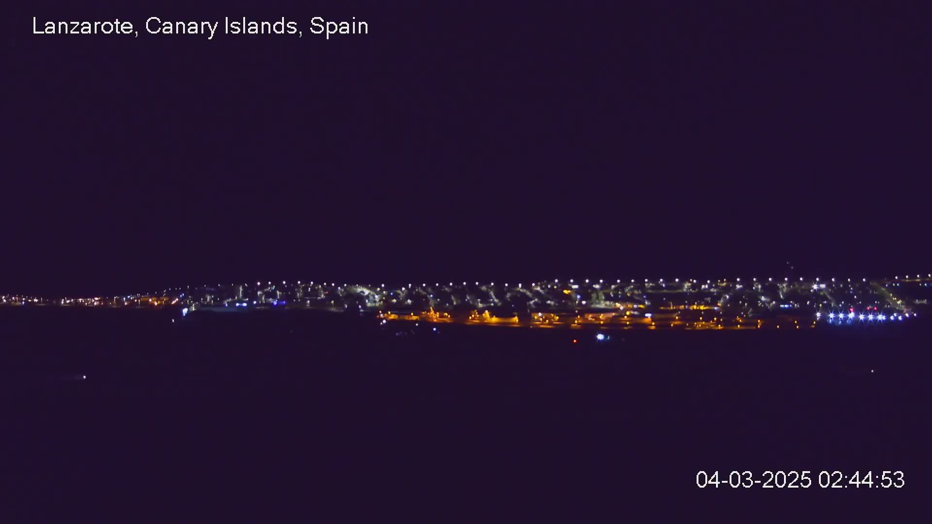 A nighttime long shot shows a line of city lights under a dark sky.
