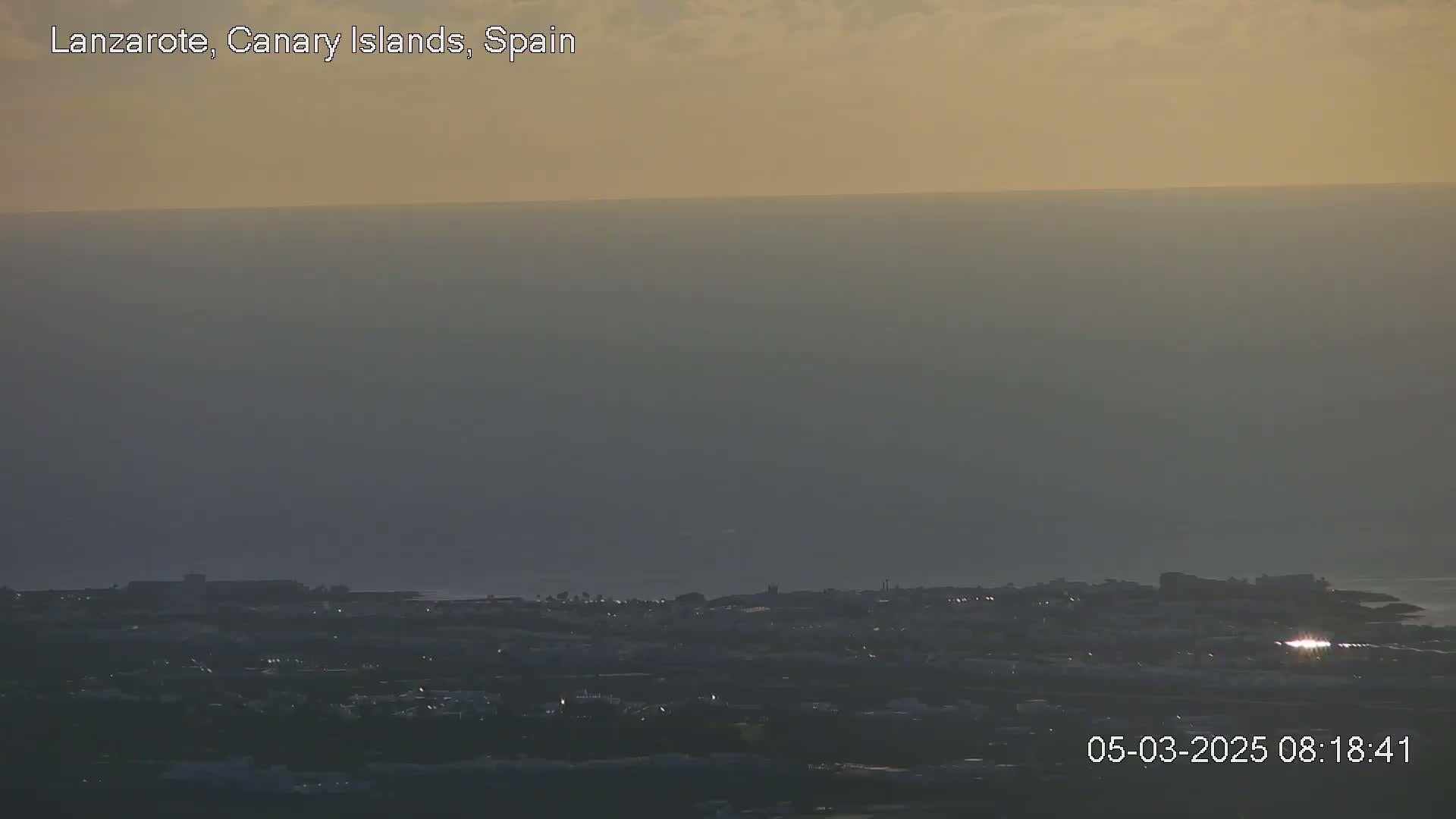 A hazy sunset illuminates a coastal town and ocean.