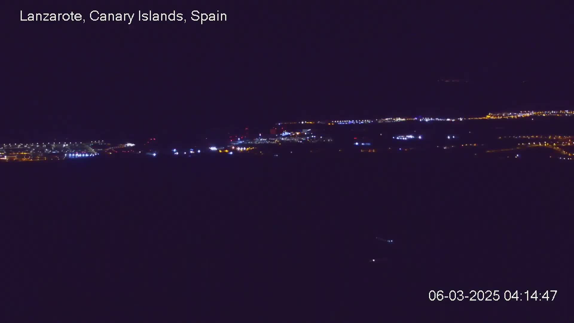 A nighttime long shot shows a distant city illuminated with scattered lights under a clear, dark sky.